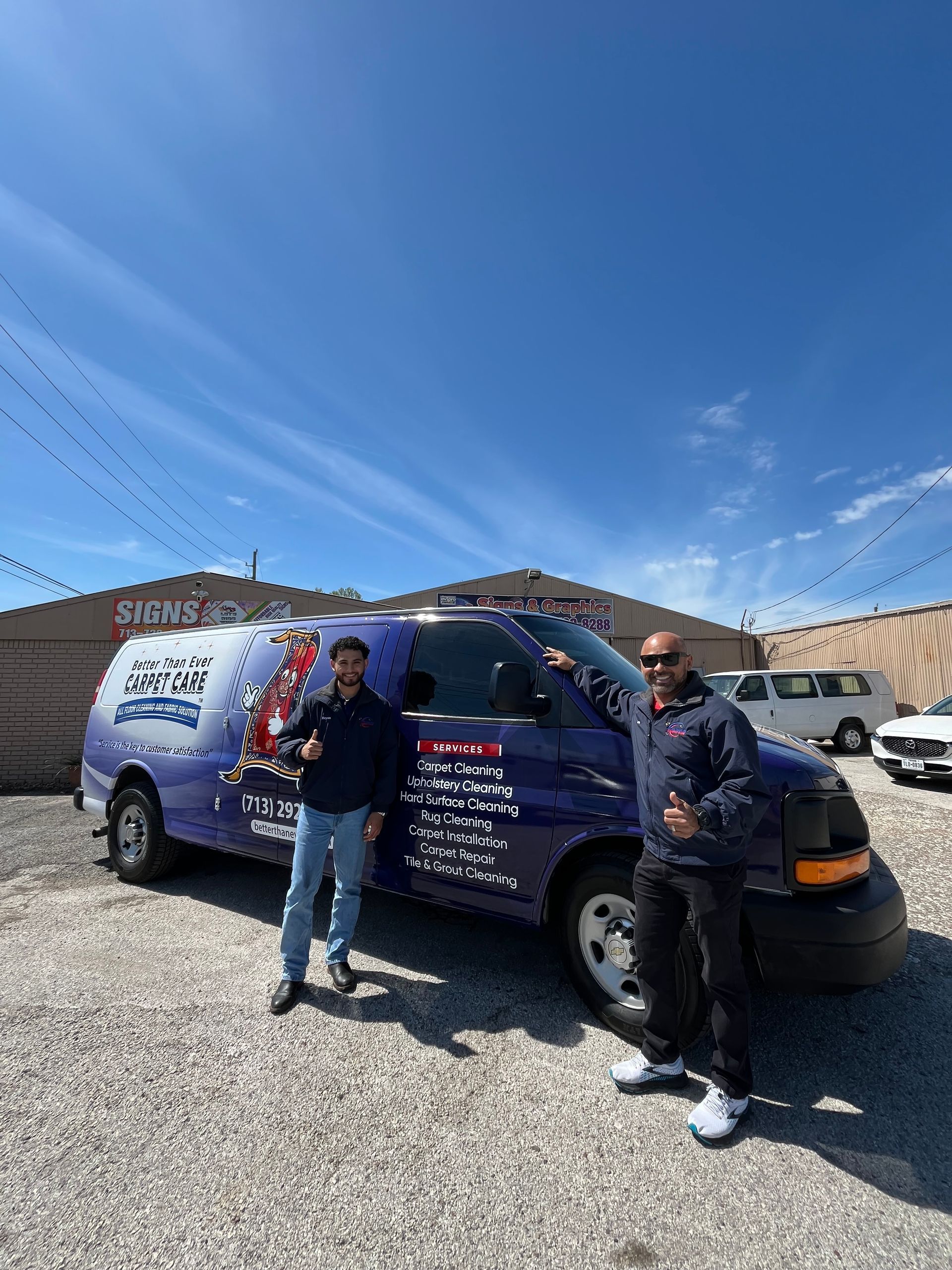 Two men stand by a purple service van. The van has business details. Sunny day, gravel lot.