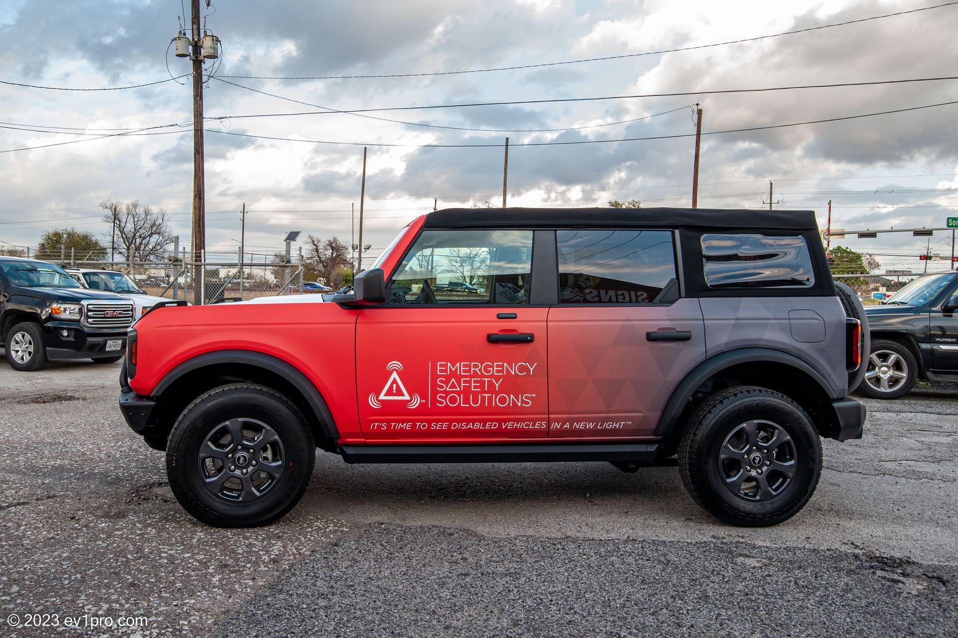 Red and black Ford Bronco SUV with company logo parked on gravel.