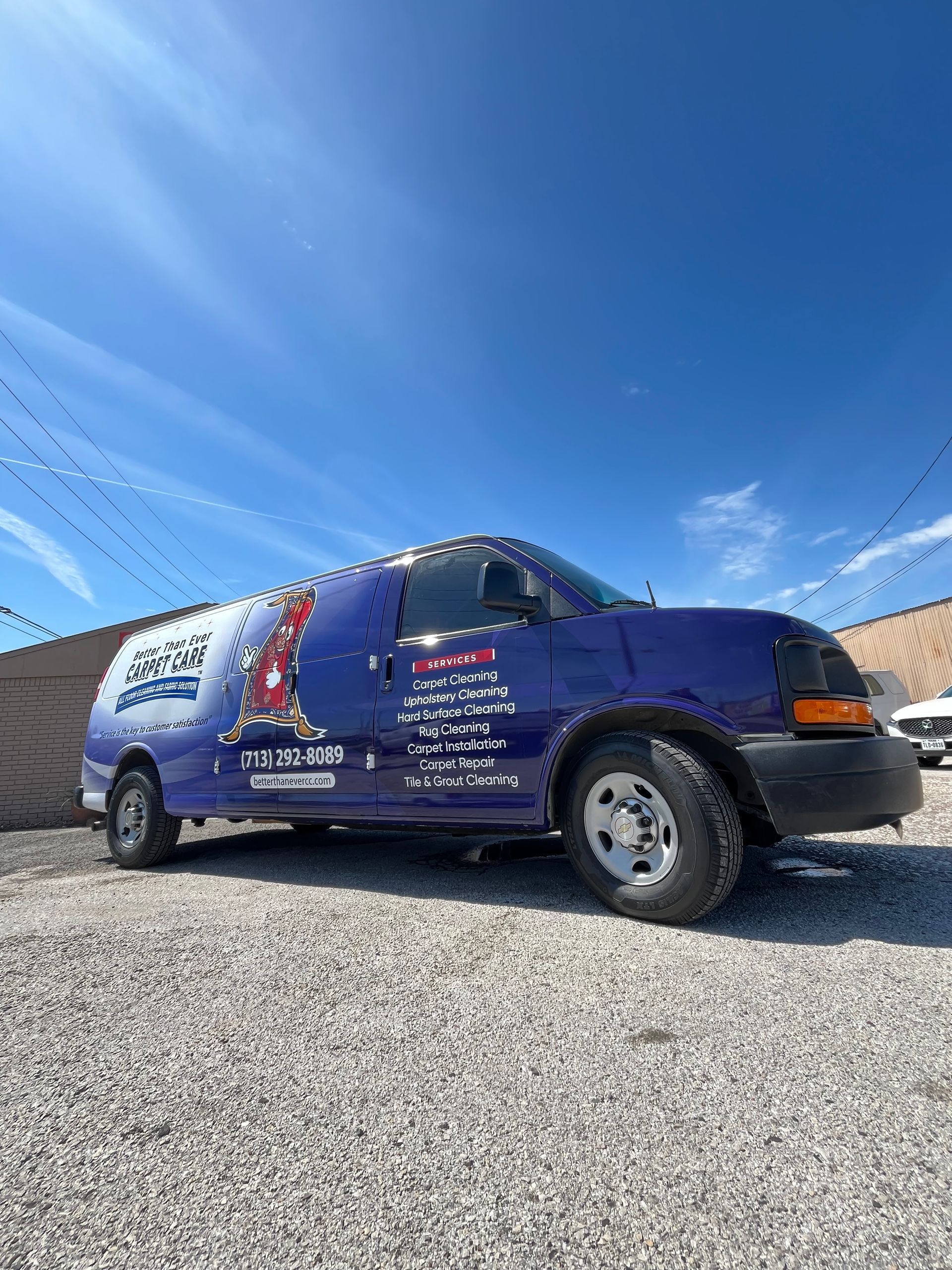 Blue van with business logo parked on gravel under a blue sky with white clouds.