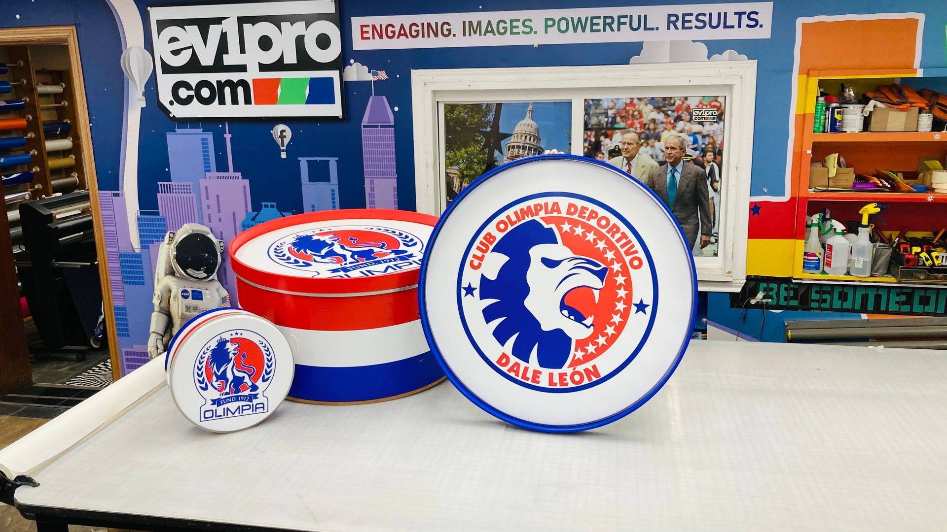Three round signs, red, white, and blue, with an eagle logo, sit on a white surface in front of a colorful backdrop.