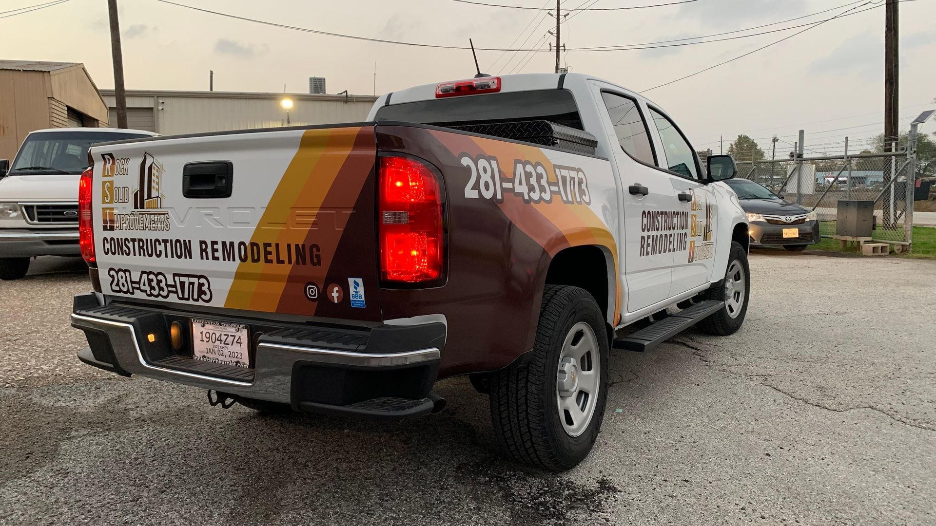 White pickup truck with business graphics parked on pavement; brown, tan, and orange color scheme.