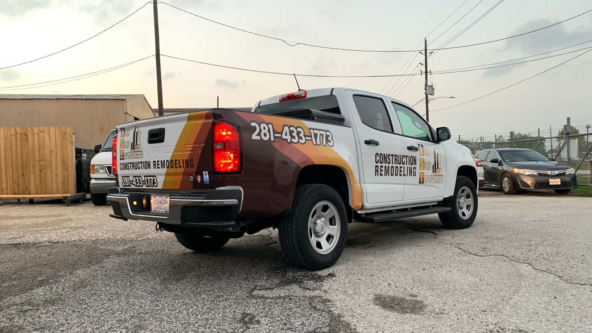 White Chevrolet truck with company logo parked on asphalt. Brown and orange stripes on the truck bed.