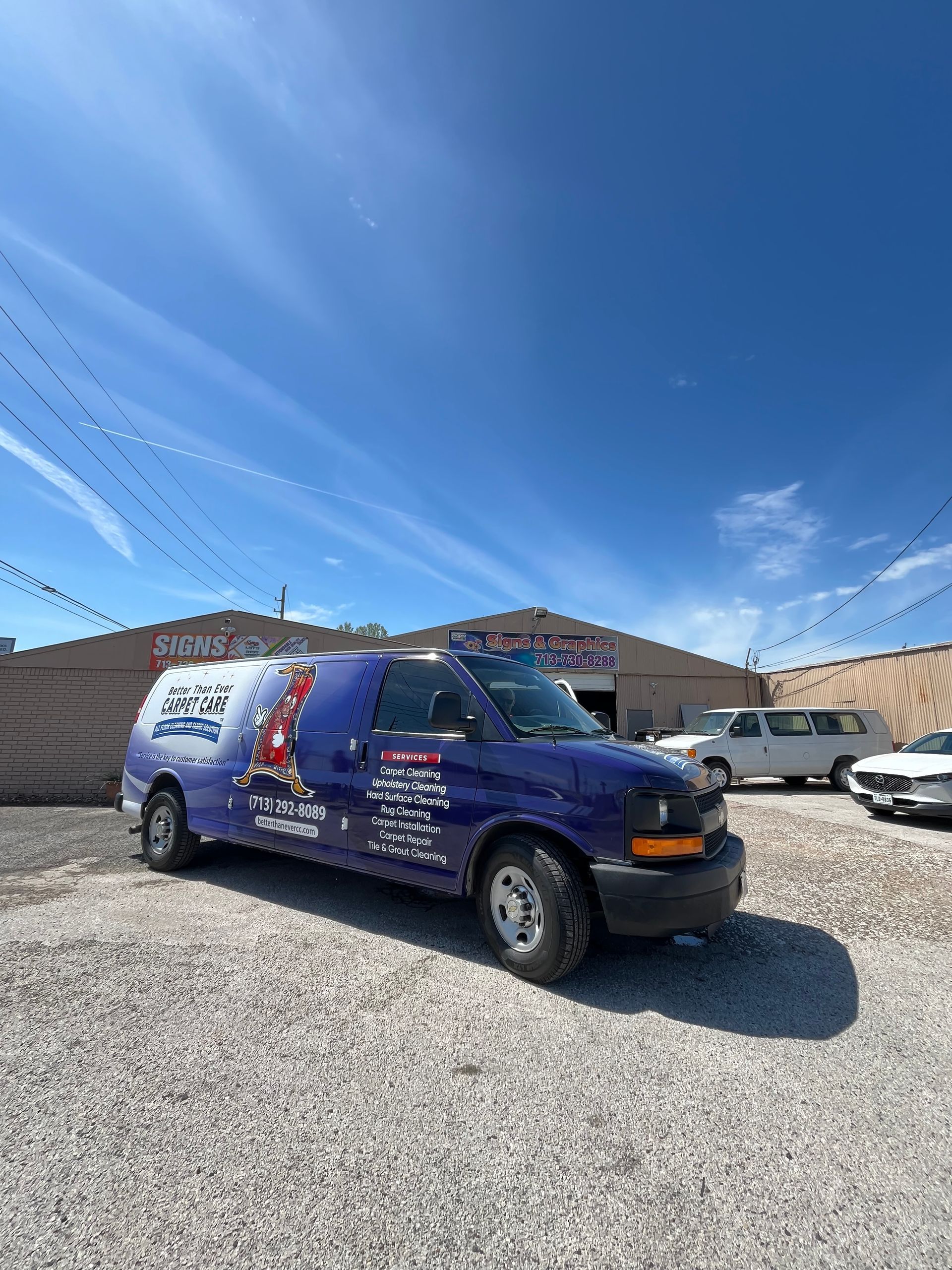 Blue work van parked in a gravel lot under a blue sky. The van has business logos on its side.