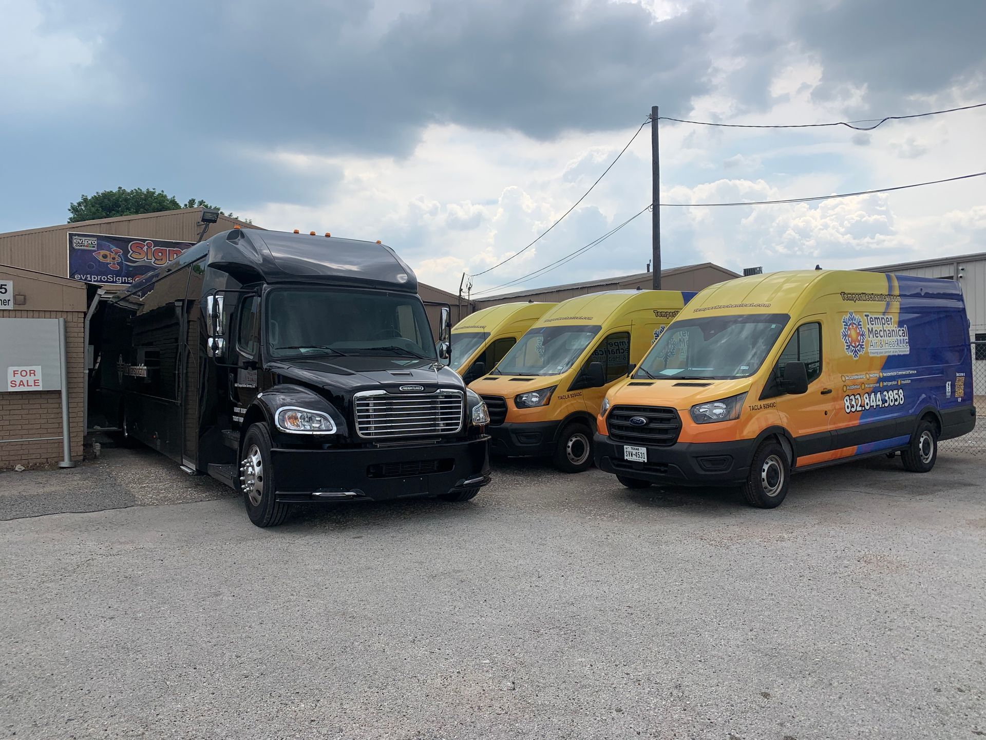 Black bus and three yellow vans parked outside a brick building under a cloudy sky.