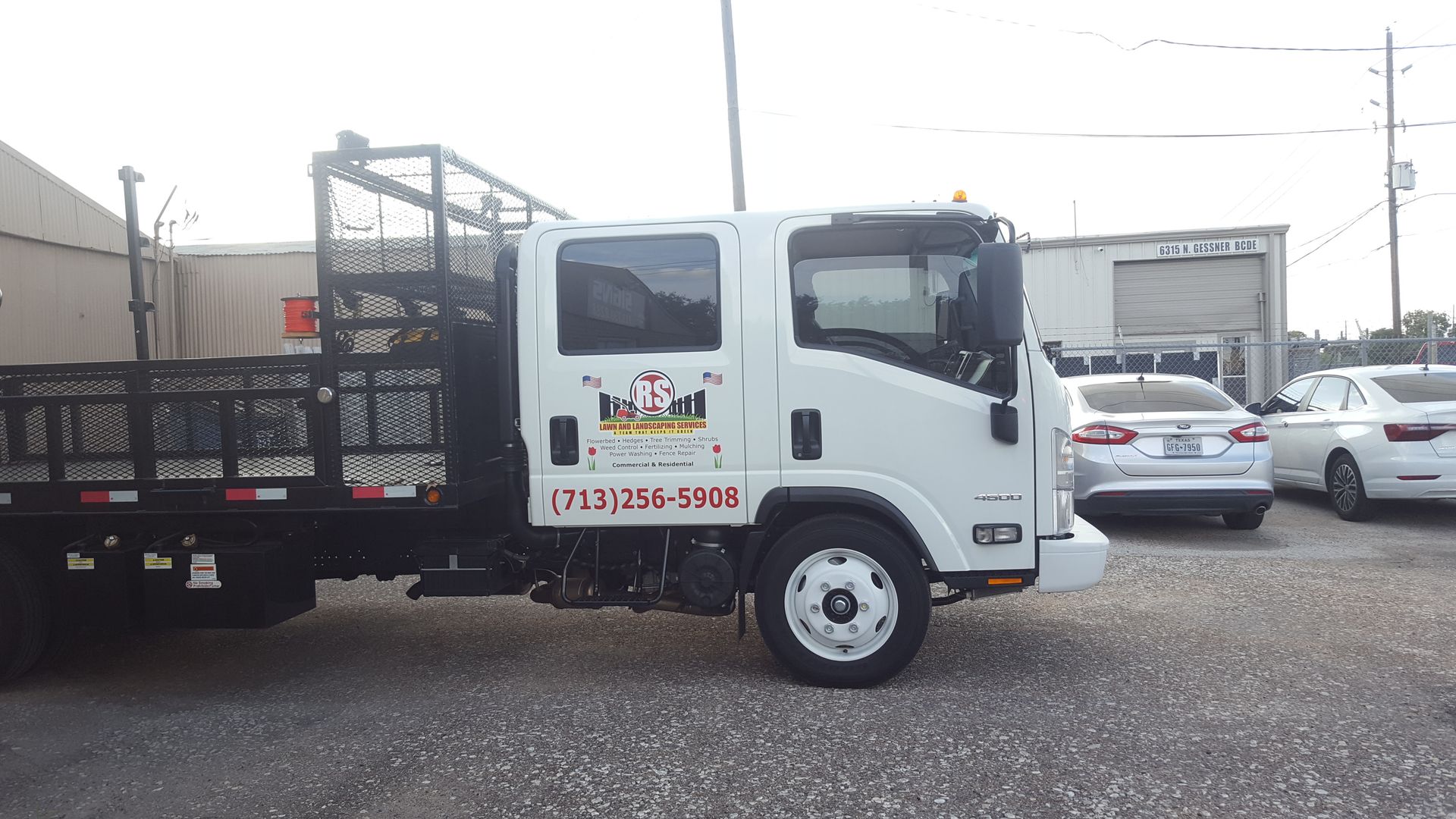 White work truck with black flatbed, parked in front of buildings, under a cloudy sky.