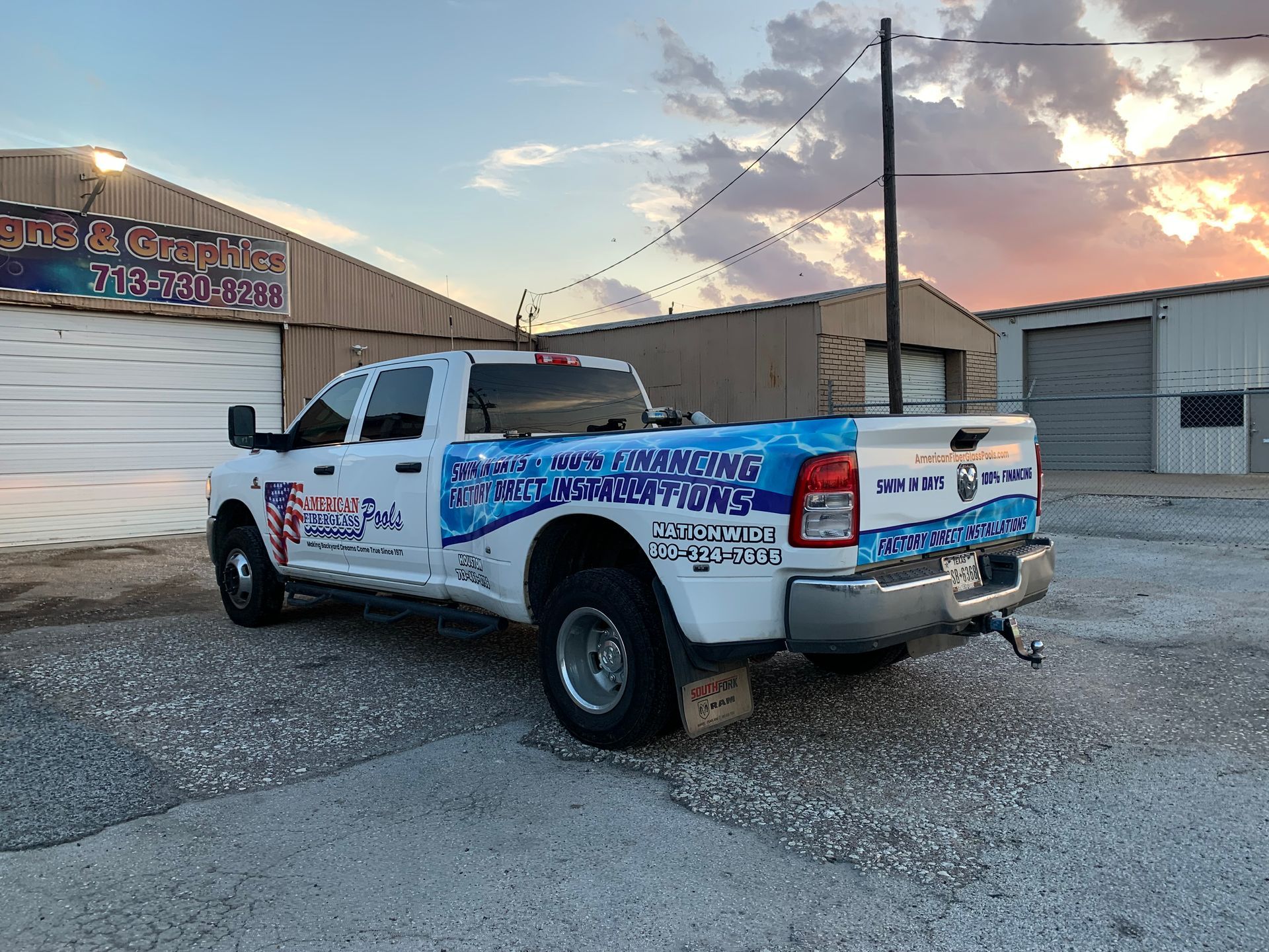 White pickup truck with business graphics parked in front of a building. Sunset in background.