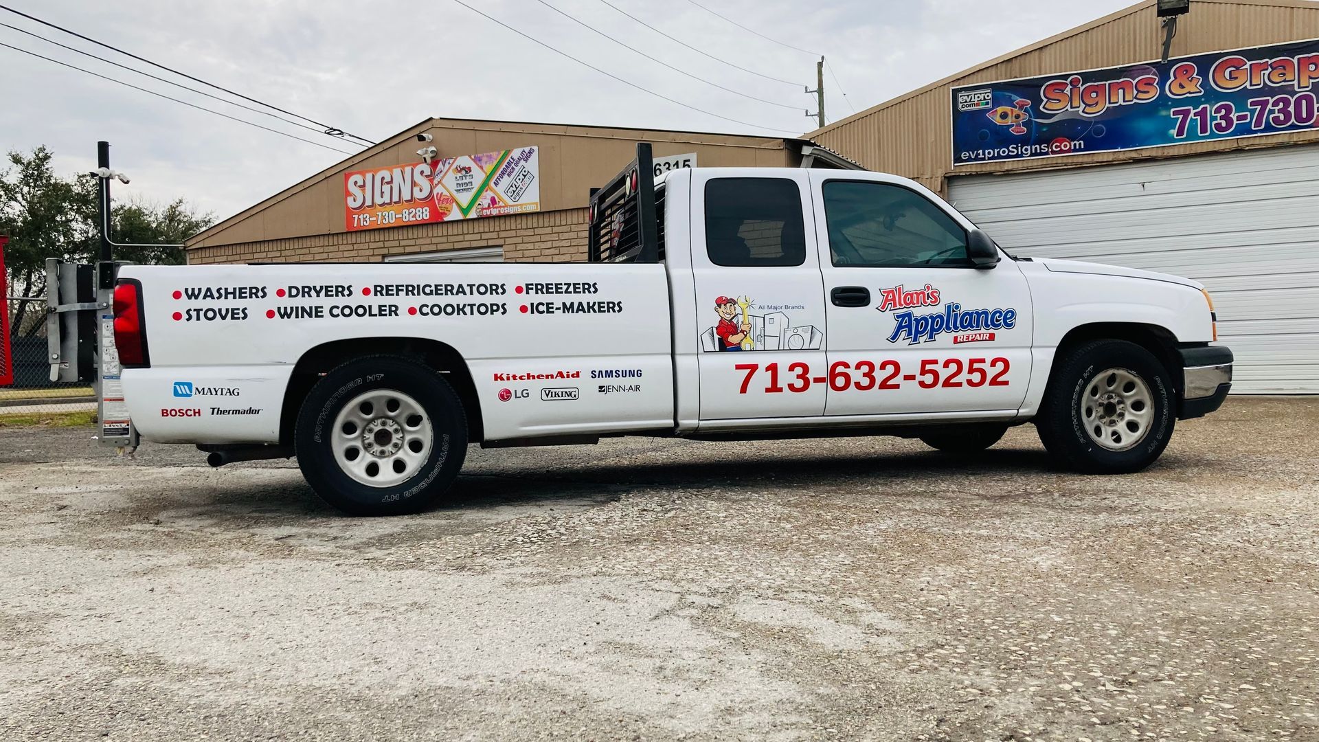 White pickup truck with business logos and phone number parked in front of a building.