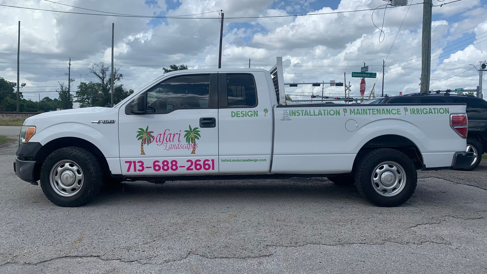 White pickup truck with business logo and phone number, parked outside.