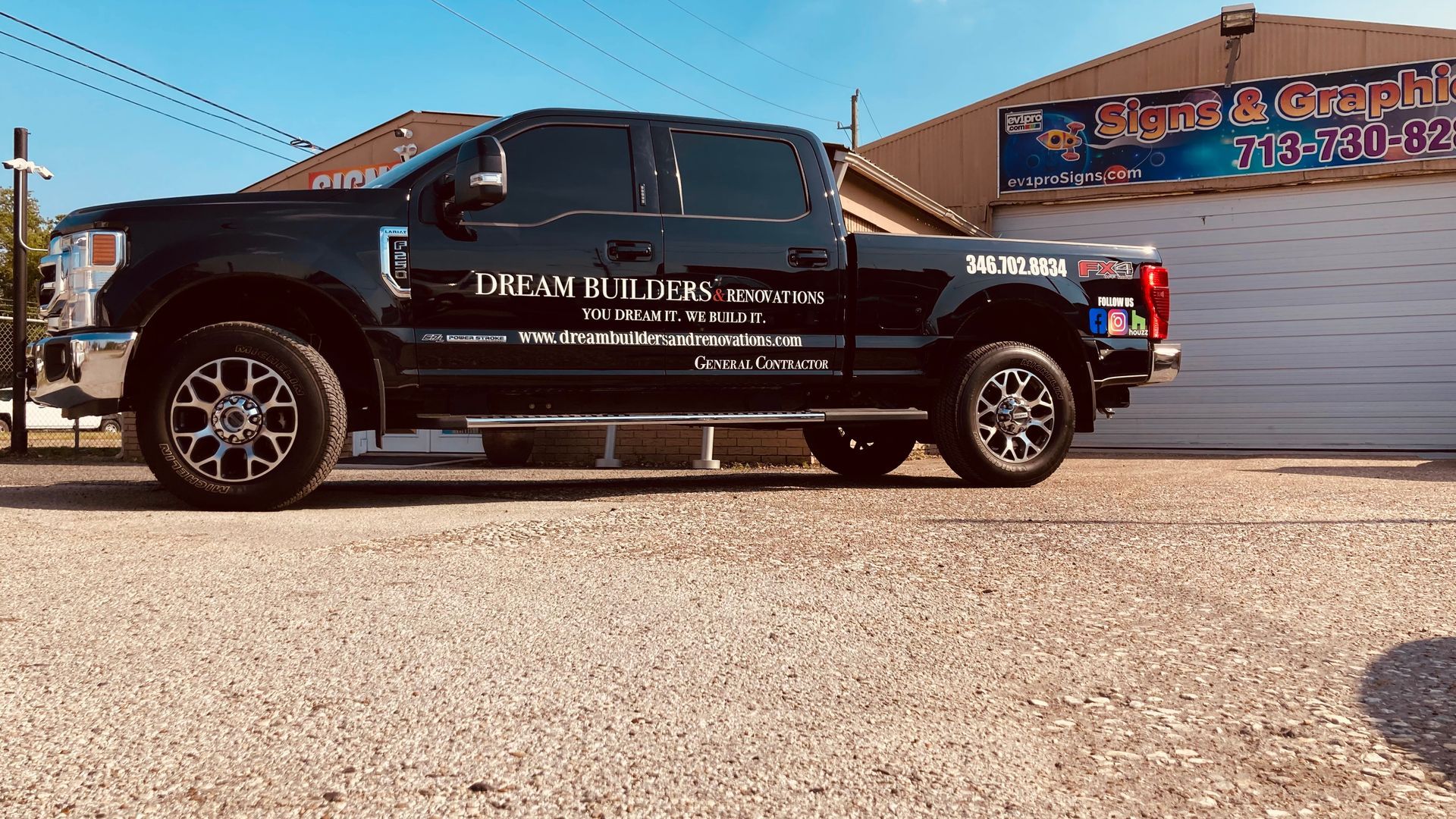Black Ford truck with company logo parked outside a building on a gravel lot.
