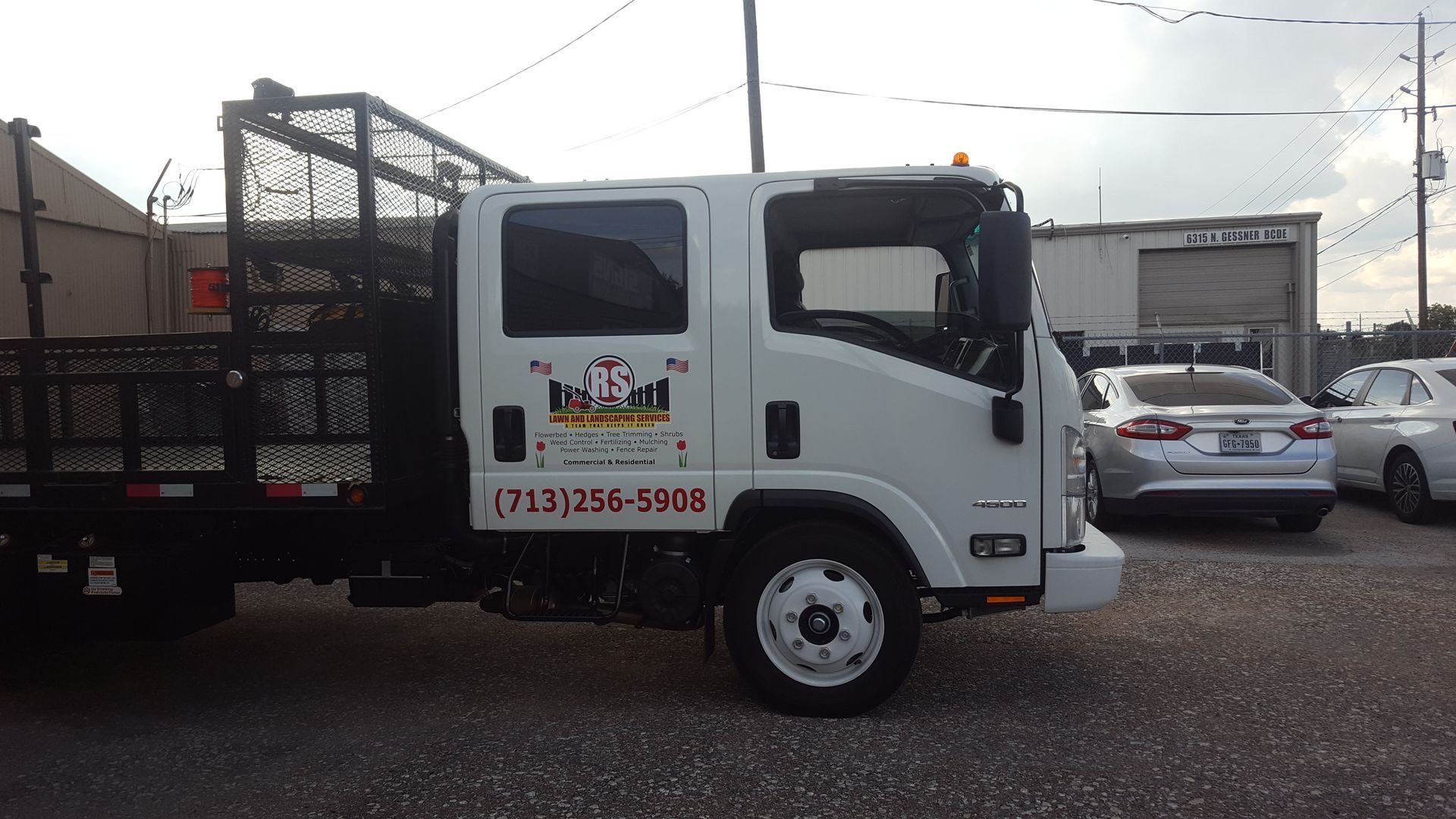 White work truck with logo, black bed, and phone number on the side, parked outside.