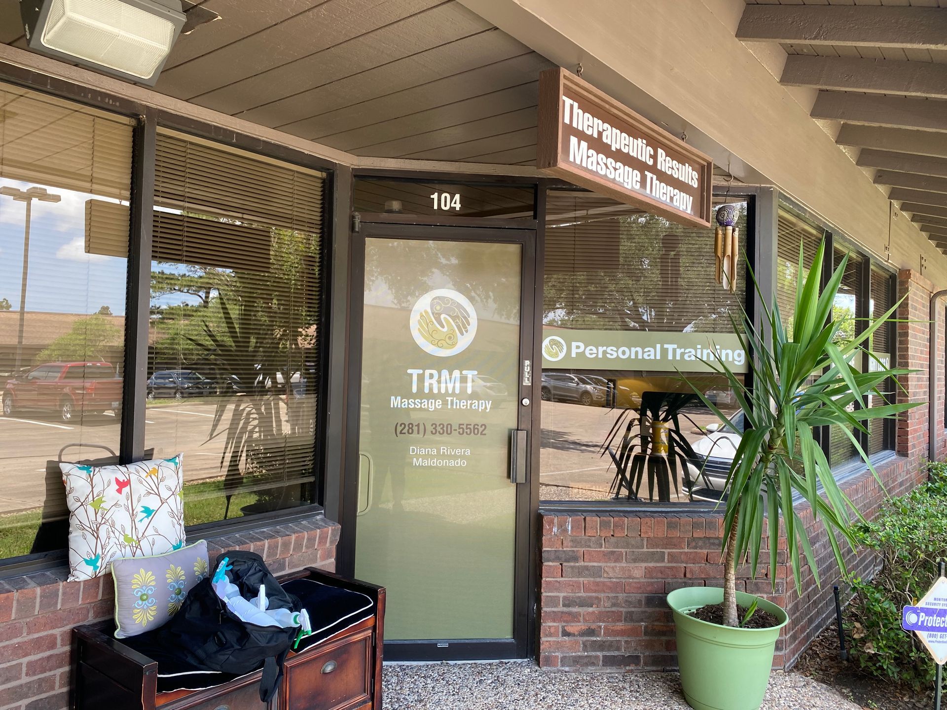 Exterior of a massage therapy office with a brick facade. Door and window display, potted plant, and outdoor seating.