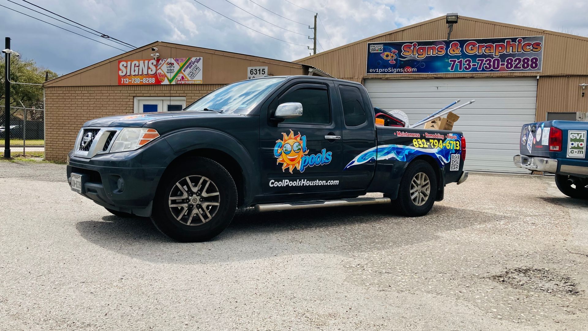 Dark gray pickup truck with business graphics parked in front of a brick building.