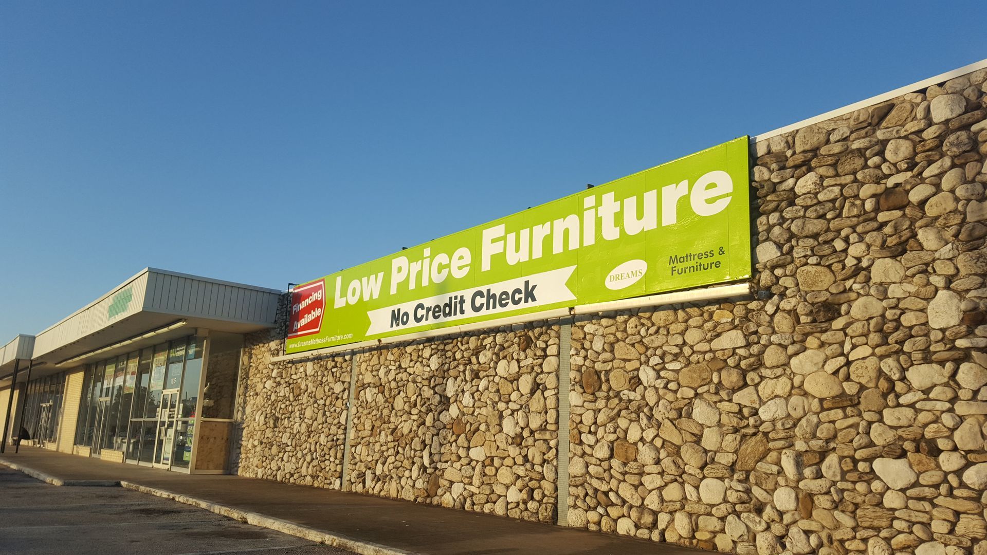 Low Price Furniture store exterior with green and red sign on stone wall, under a blue sky.