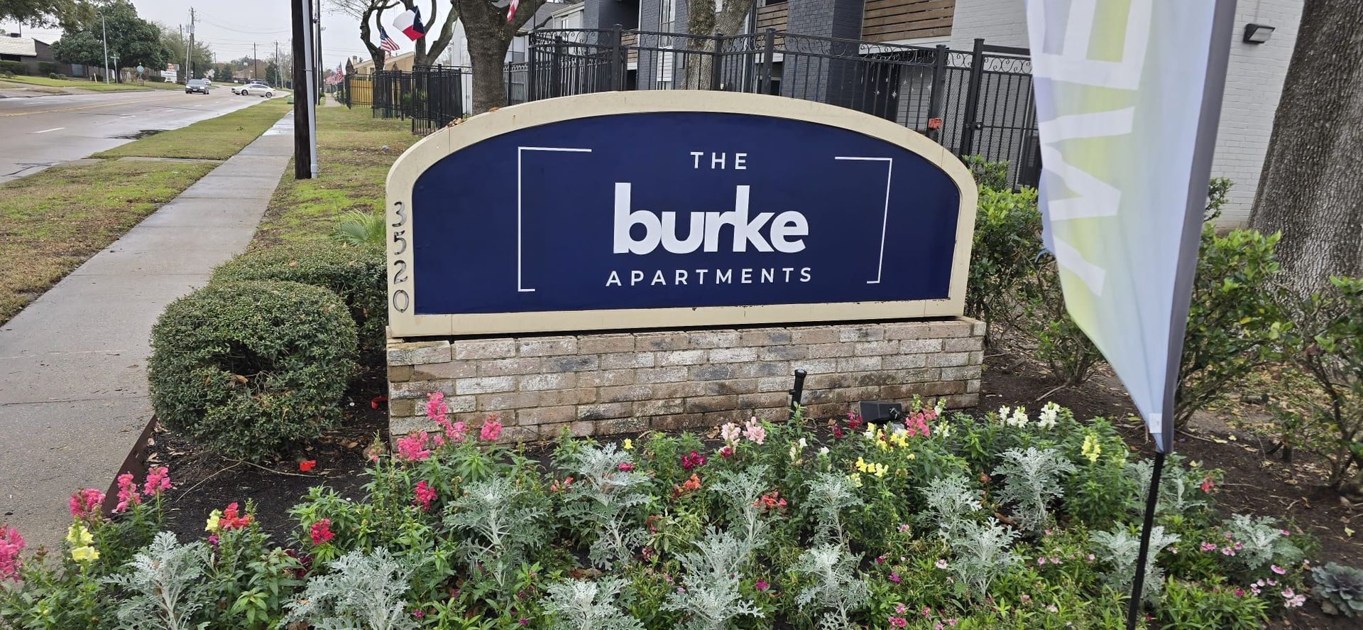 Sign for The Burke Apartments with flower bed in front.