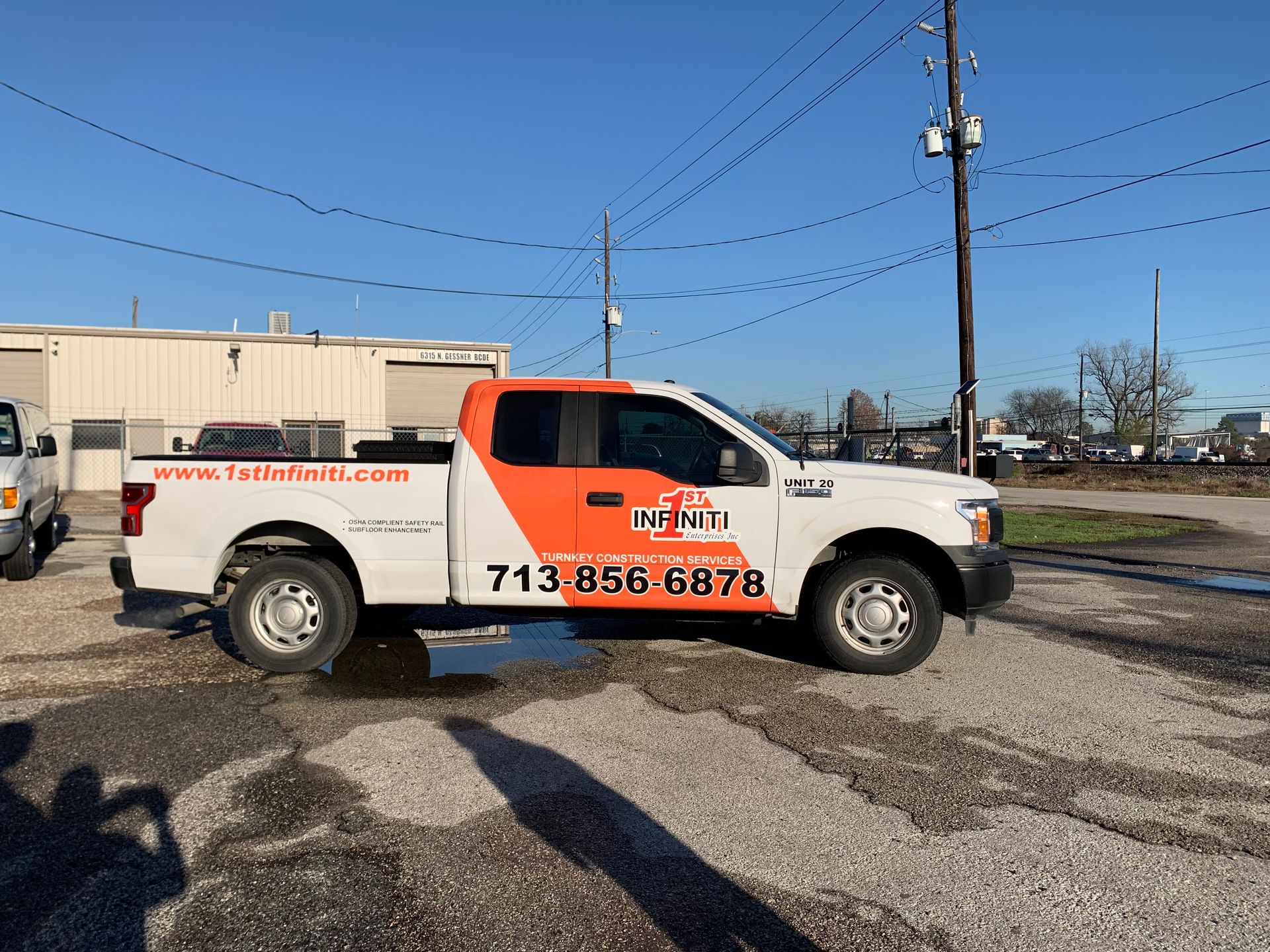White Ford pickup truck with orange logo and phone number, parked outside on a cloudy day.
