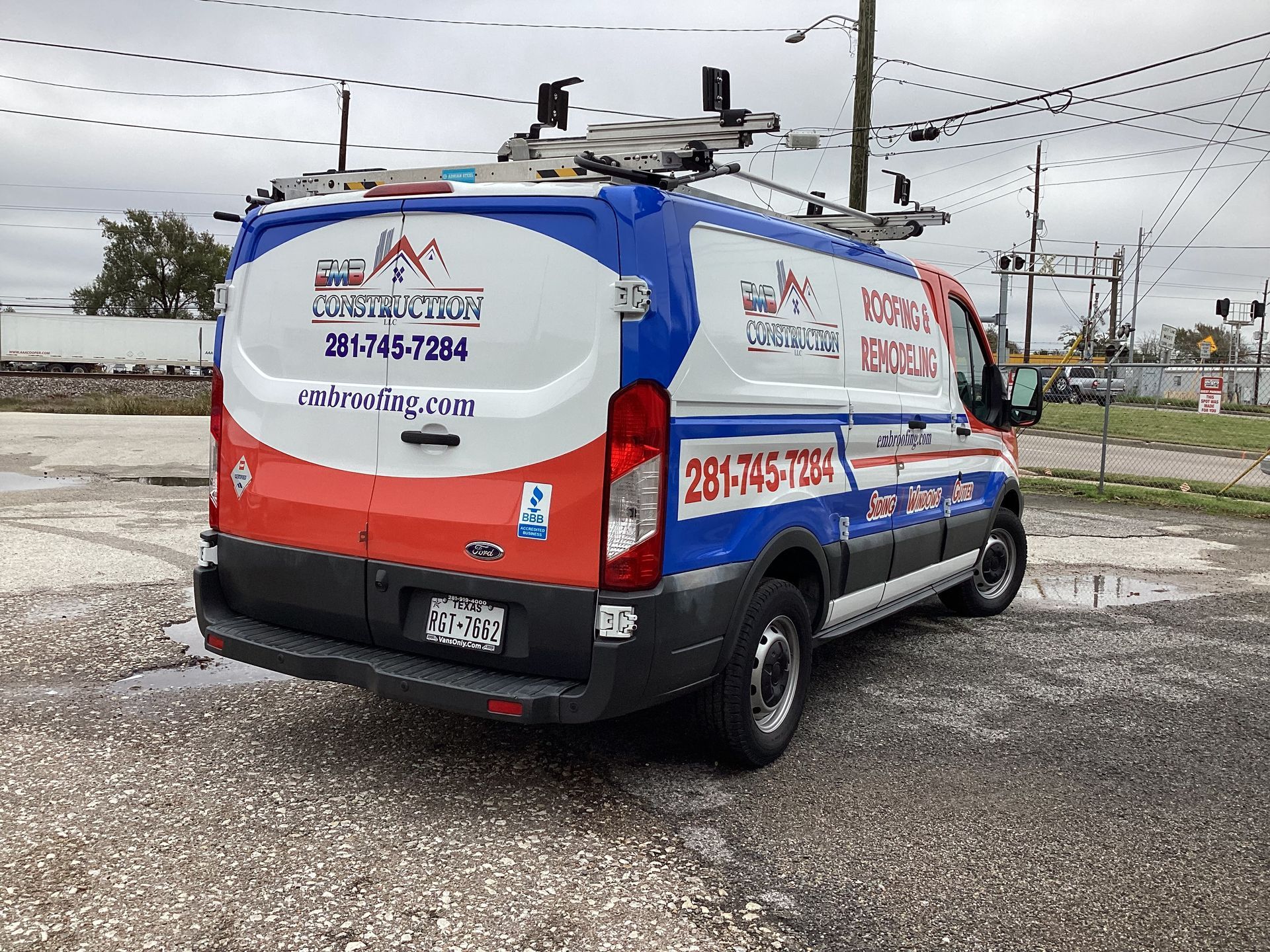 Blue, red, and white roofing van with company logo parked outside.