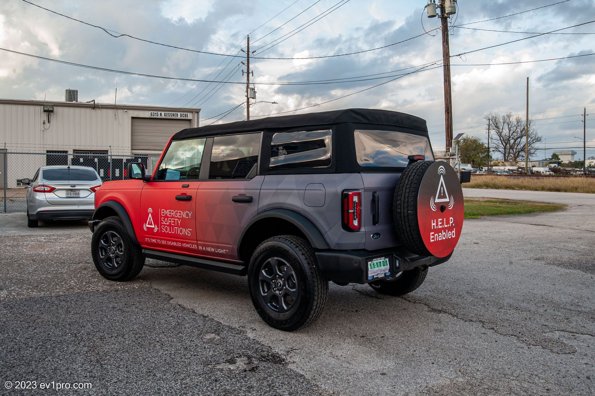 Red and gray Ford Bronco SUV parked on gravel, with a soft top.