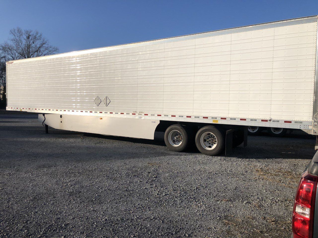 A white trailer is parked in a gravel lot next to a truck.