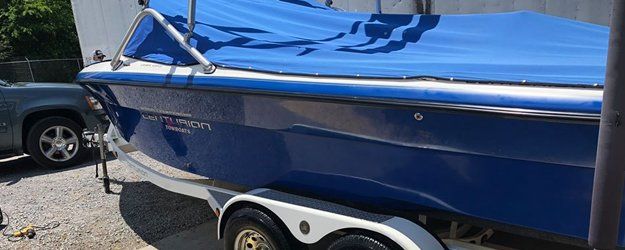 A blue boat is sitting on a trailer next to a car.