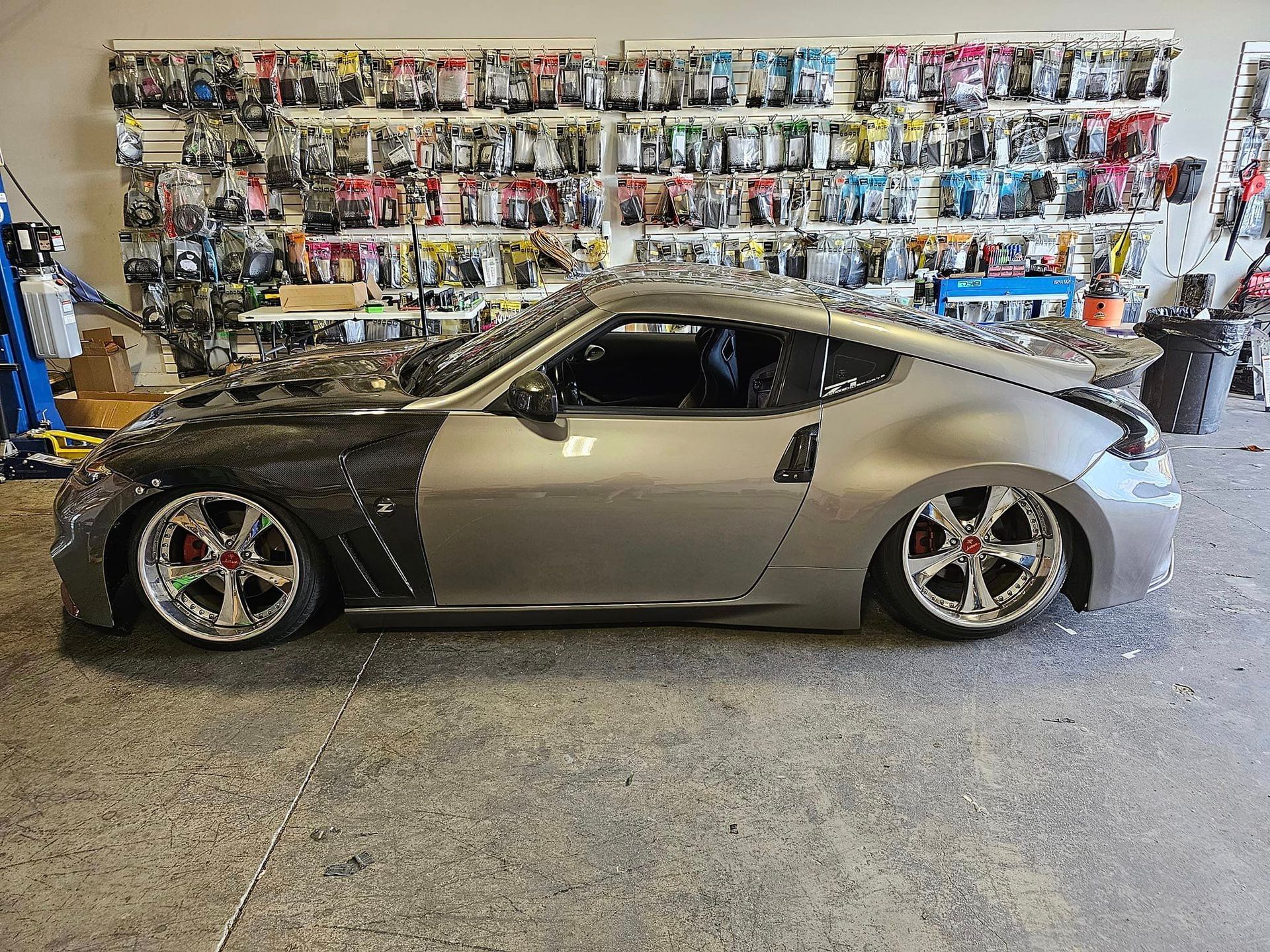A silver sports car is parked in a garage in front of a wall of tools.
