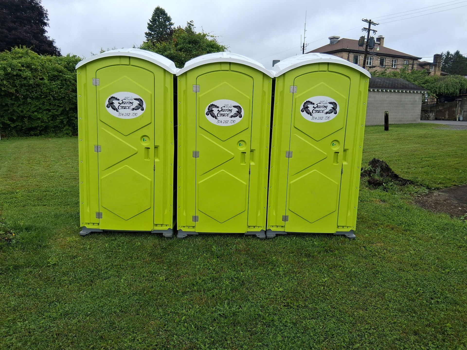 Three bright yellow portable toilets on a grassy lawn under an overcast sky.