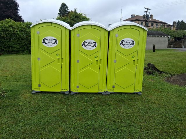 Three lime-green portable toilets on a grassy field outdoors