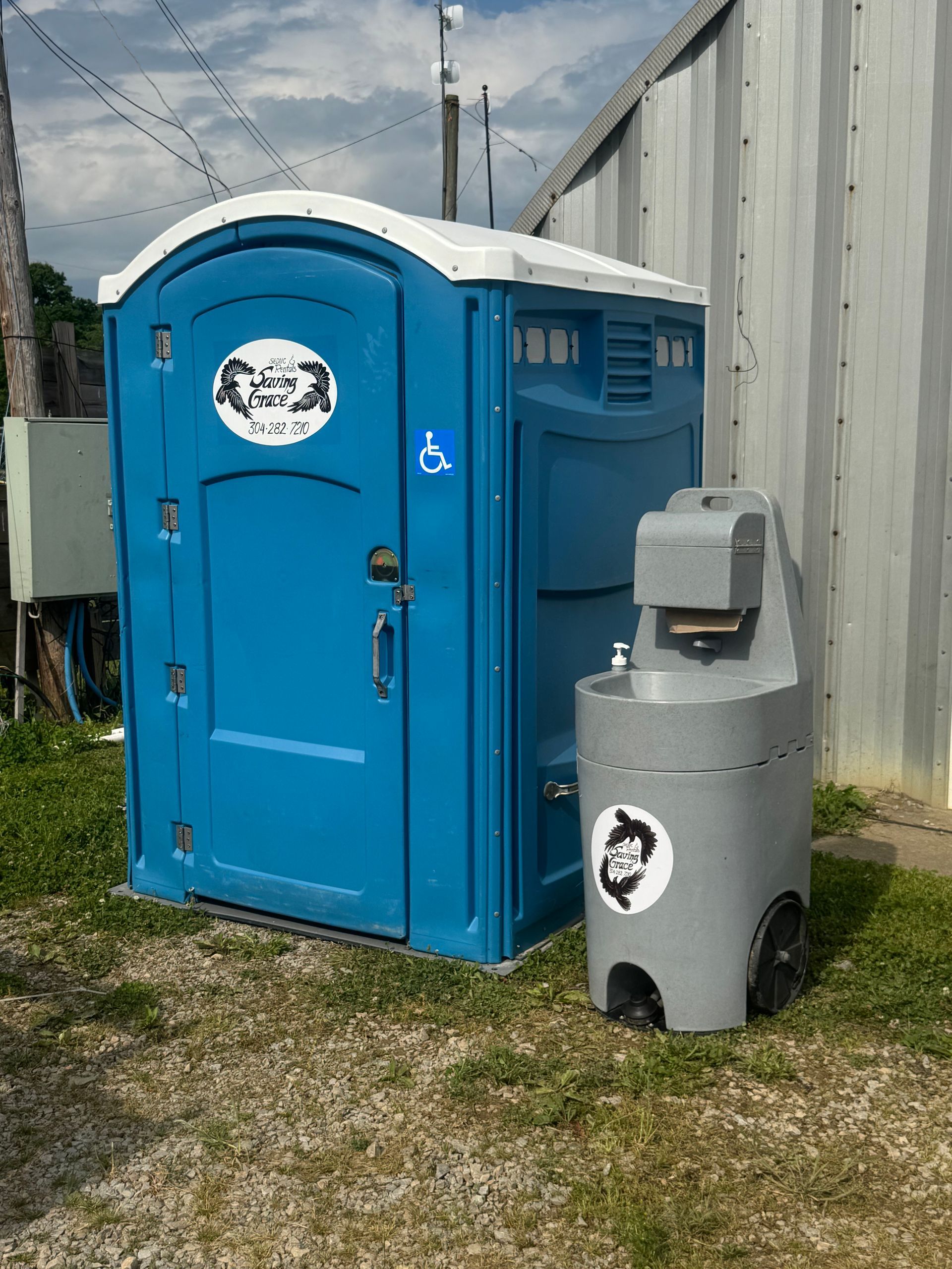 Blue portable toilet with attached gray handwashing station outdoors near a building.