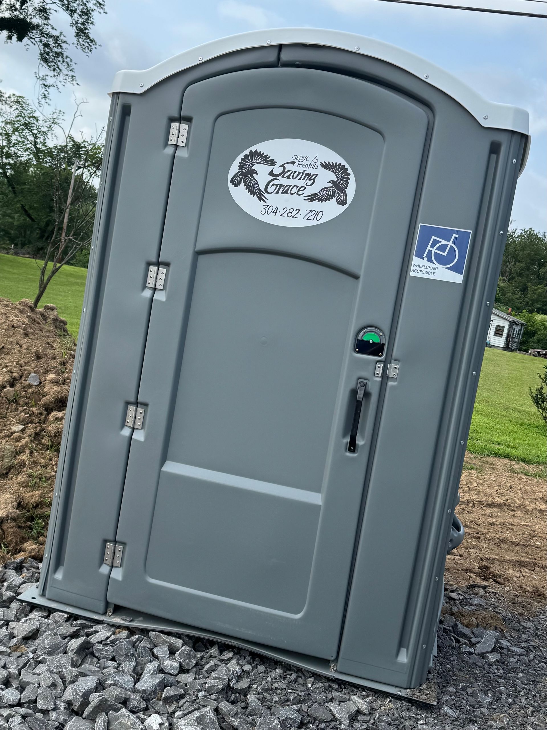 Gray portable toilet on gravel outdoors, with a blue handicap sign on the side.