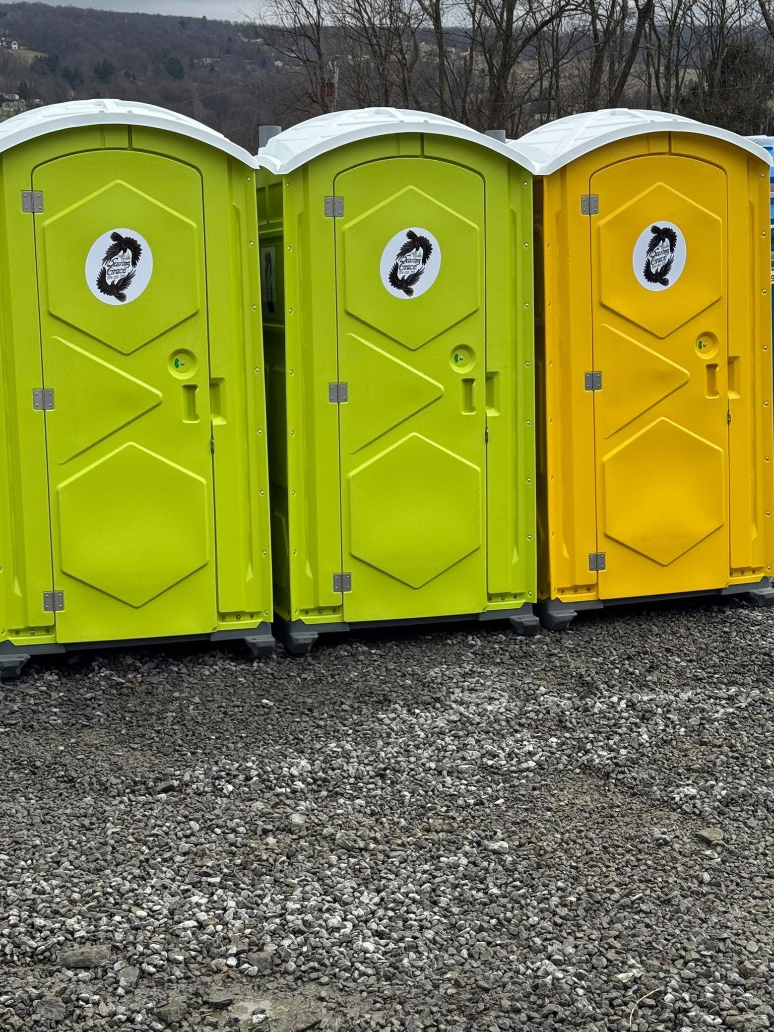 Three portable toilets: two lime green and one yellow on gravel outdoors.