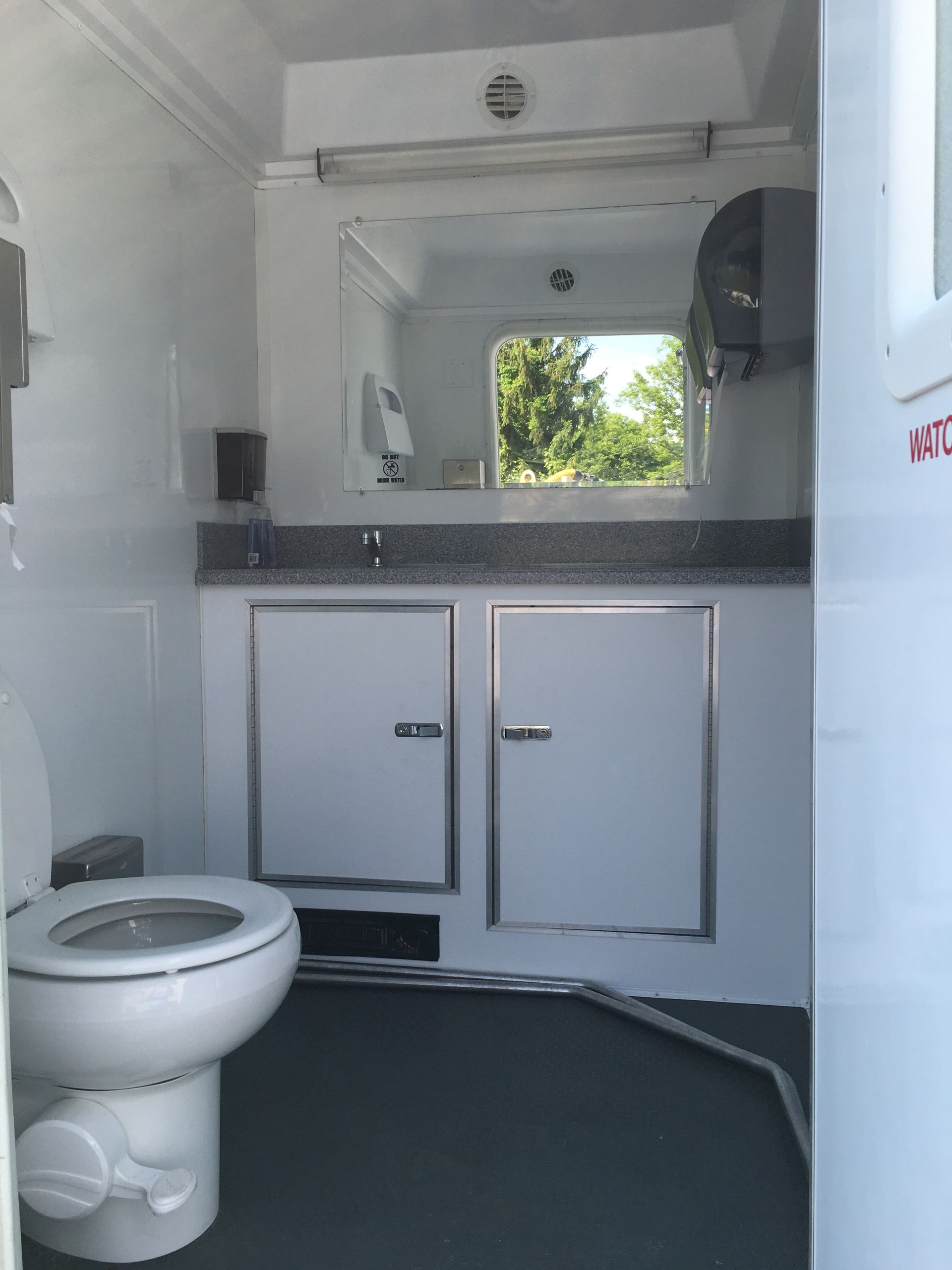 Compact bathroom with toilet, sink cabinet, mirror, and dark floor, seen from the doorway