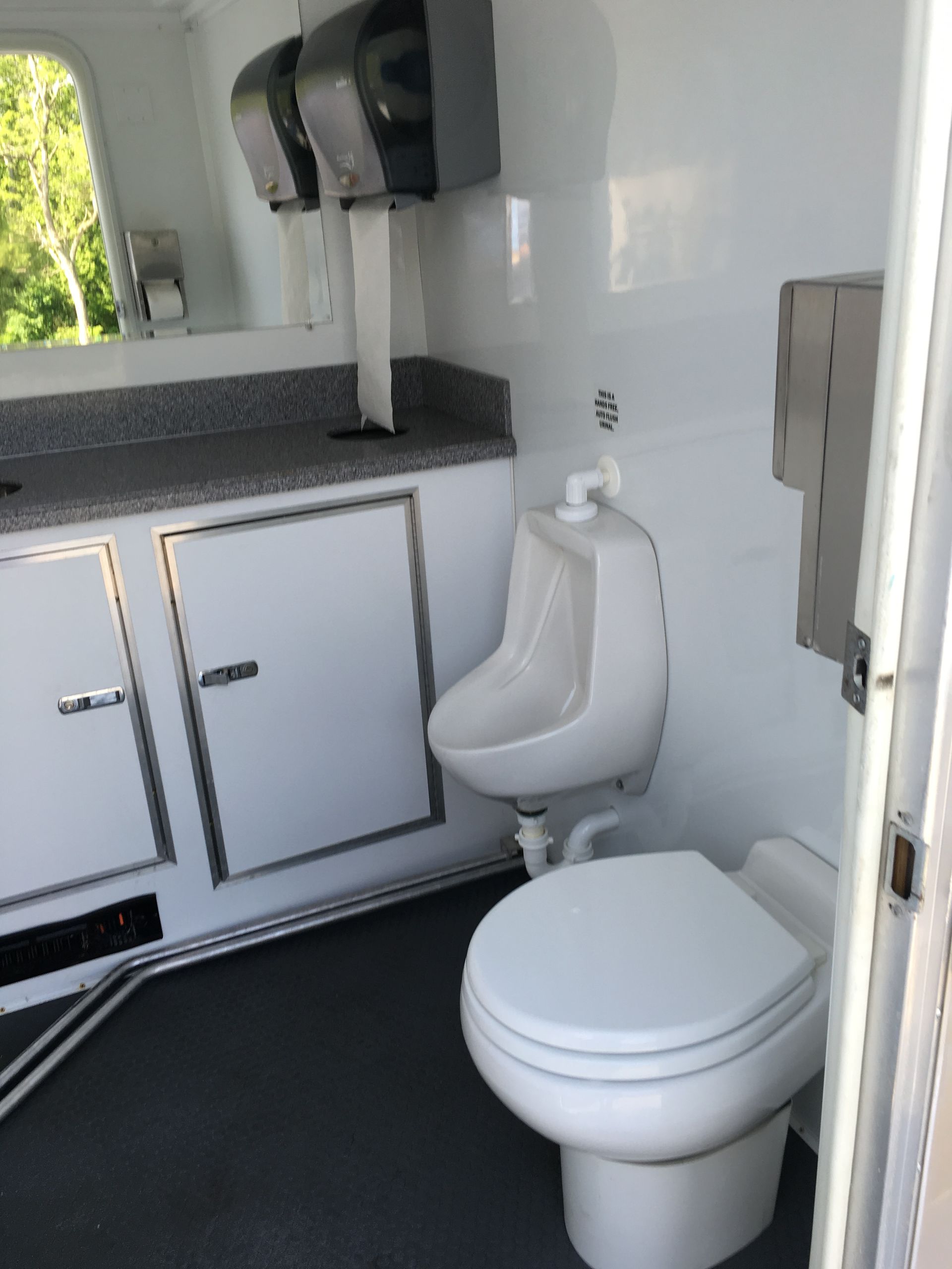 Compact camper bathroom with toilet, urinal, and sink cabinets in a white interior