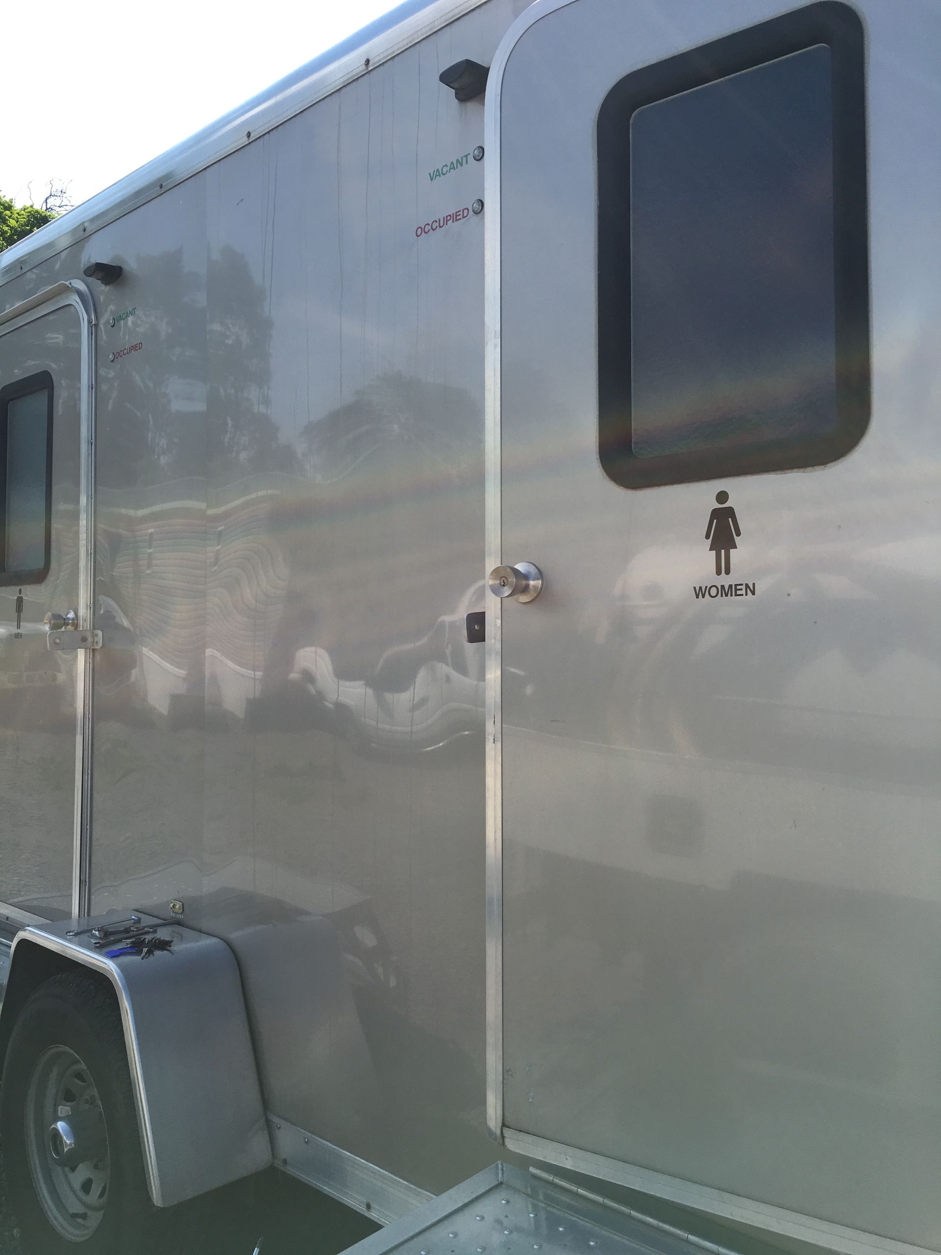 Silver enclosed trailer with black windows and a side door, parked outdoors.