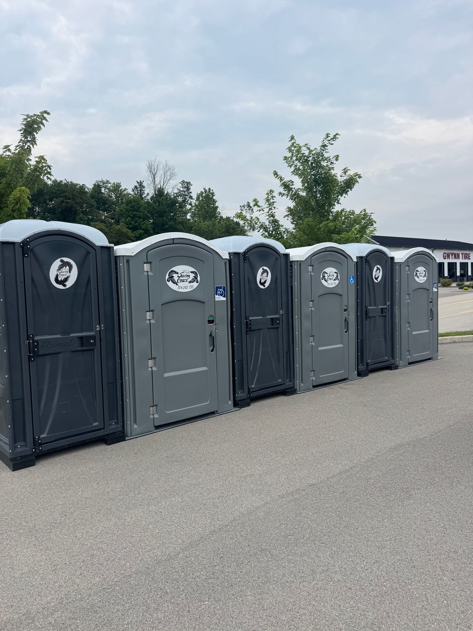 Several portable toilets lined up on a gravel lot under a cloudy sky