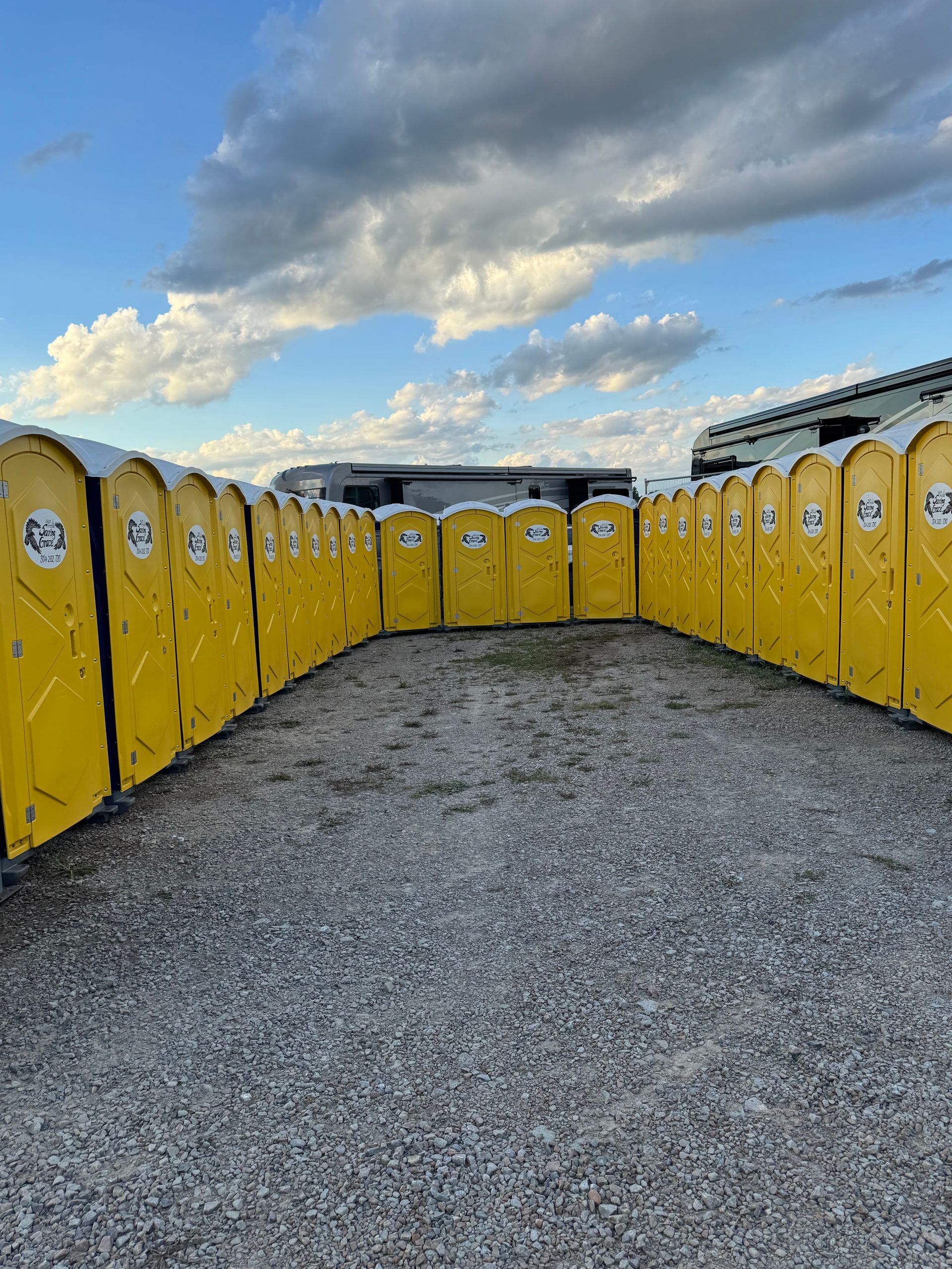 Yellow portable toilets lined up outdoors on gravel under a cloudy sky