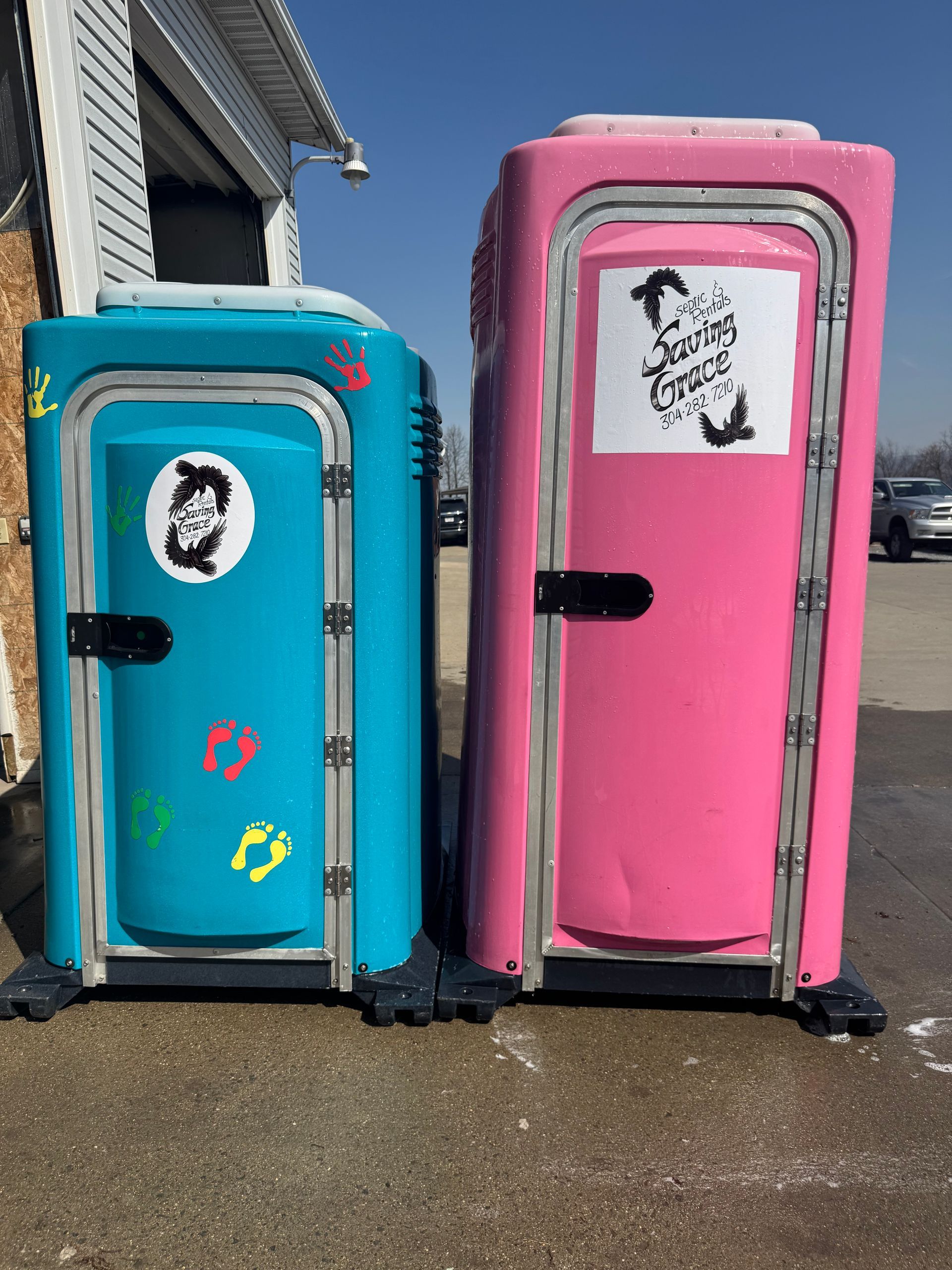 Two colorful portable toilets, teal and pink, standing outside near a building.
