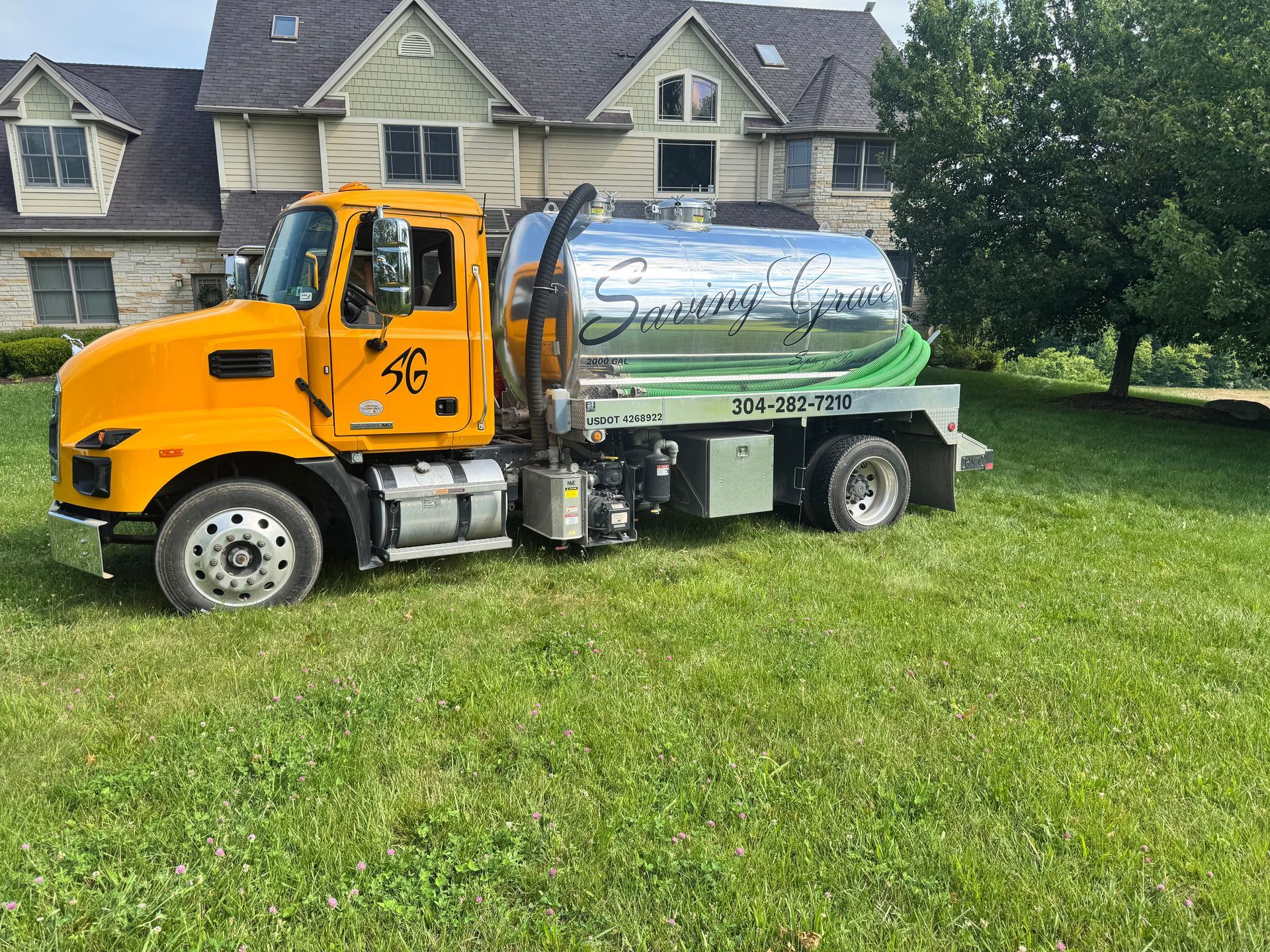 Yellow tanker truck parked on grass in front of suburban houses