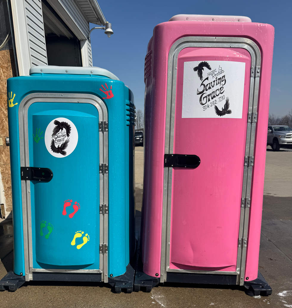 Two decorated portable toilets, one blue and one pink, standing outside on a sunny day.