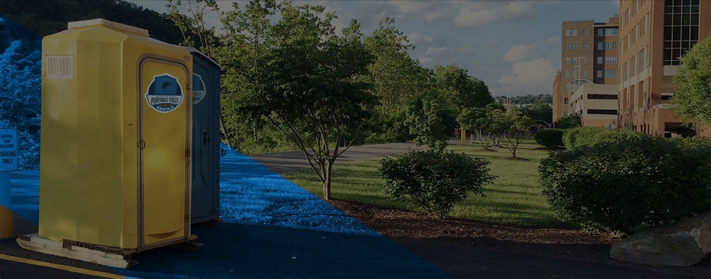 Yellow portable toilet beside blue mulch and a landscaped building entrance