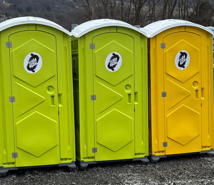 Three portable toilets in a row, two bright green and one yellow, on gravel outdoors.