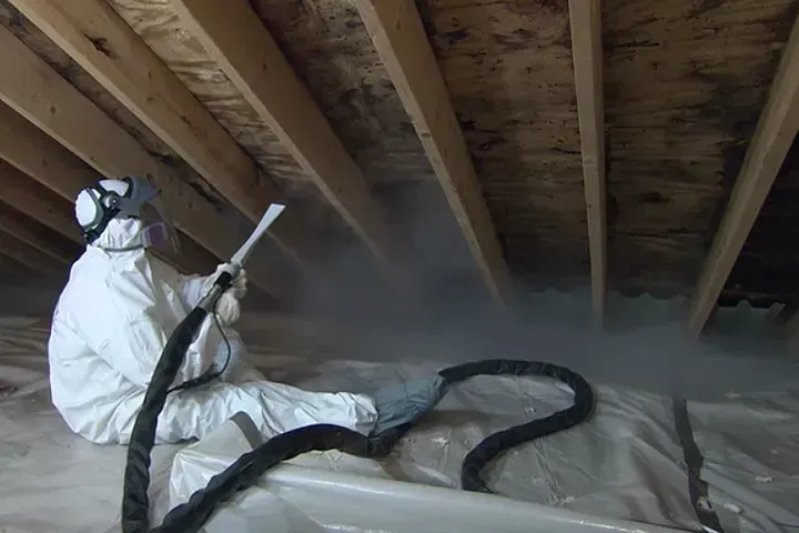 Person in protective suit spraying insulation in an attic.