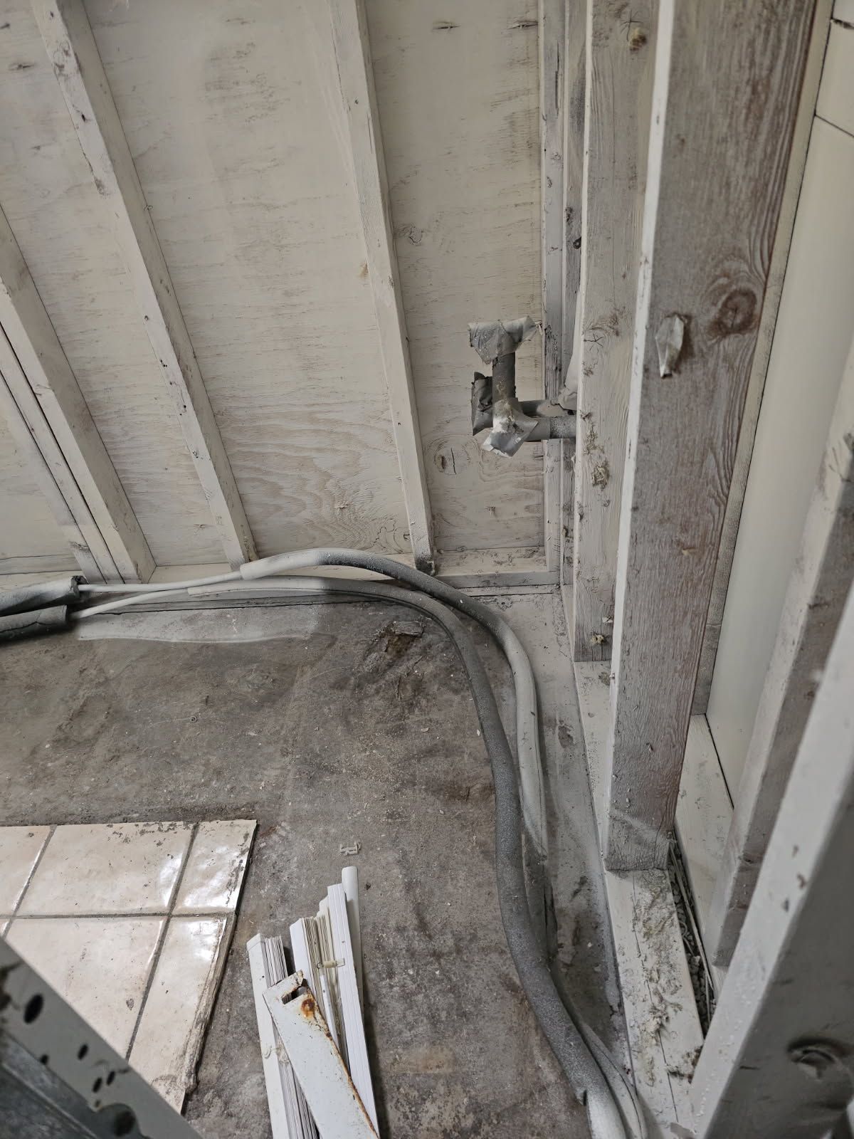 Overhead shot of white painted wood ceiling with pipes and electrical wiring running along the wall and floor.