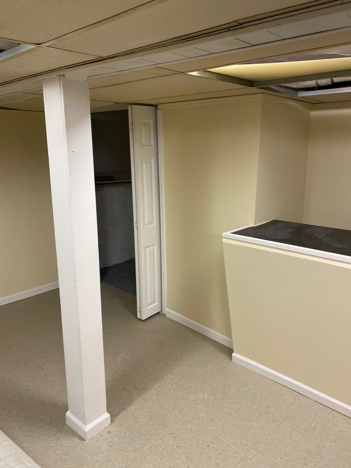Basement room with beige walls, carpet, a white support beam, and a raised platform.