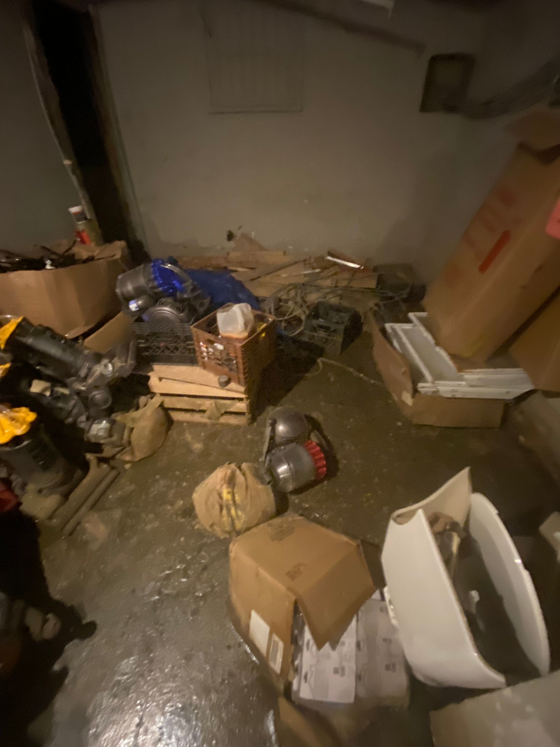 Basement with water on the floor, surrounded by boxes, wooden crates, and various items.