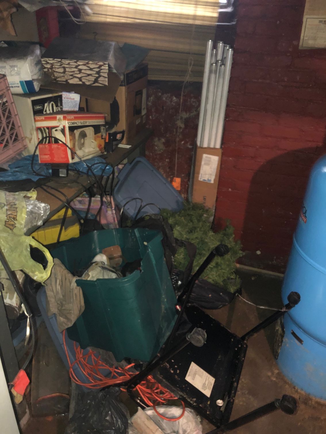Cluttered basement with boxes, furniture, Christmas tree stand, and a blue water container.