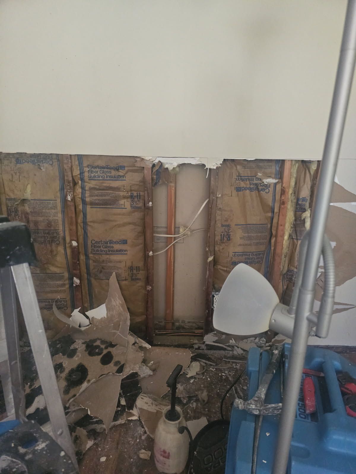 Wall damage revealing insulation and copper pipes; cleanup equipment visible.