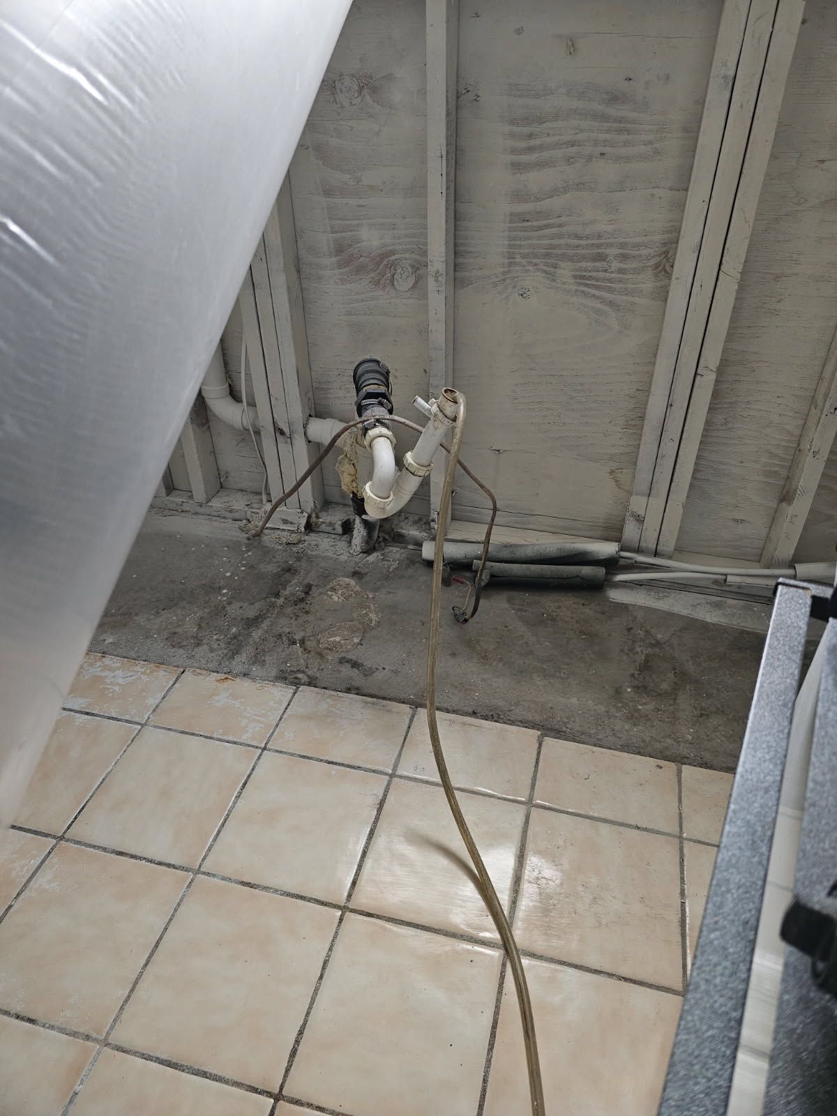 Pipes and equipment on a concrete ceiling above a tiled floor. A long brown hose extends downward.