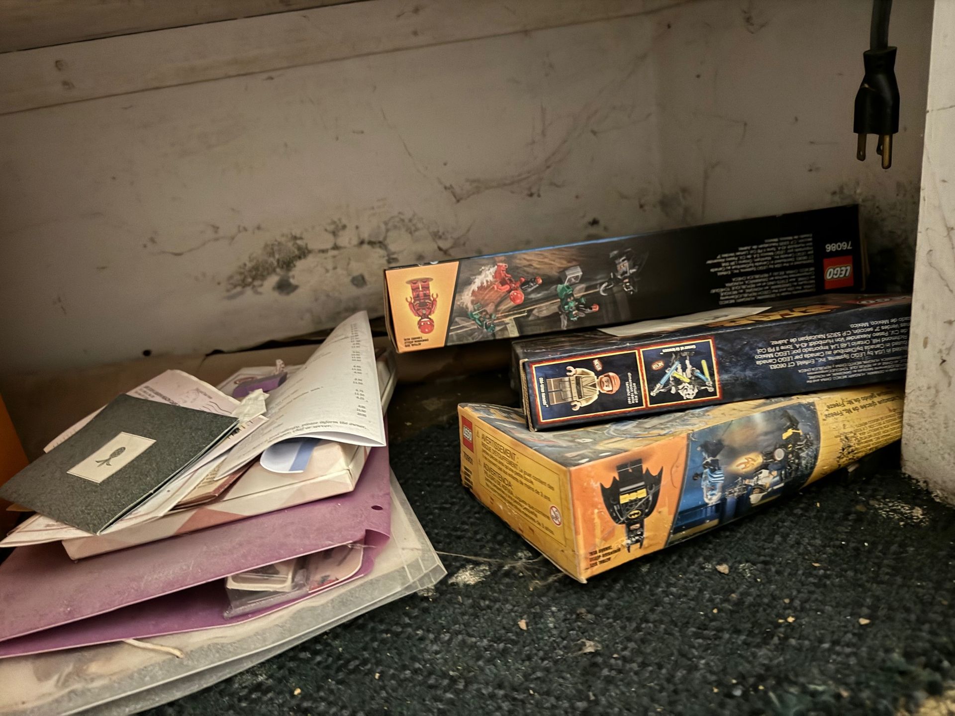 Boxes of LEGO sets and papers in a cluttered, dusty cabinet.