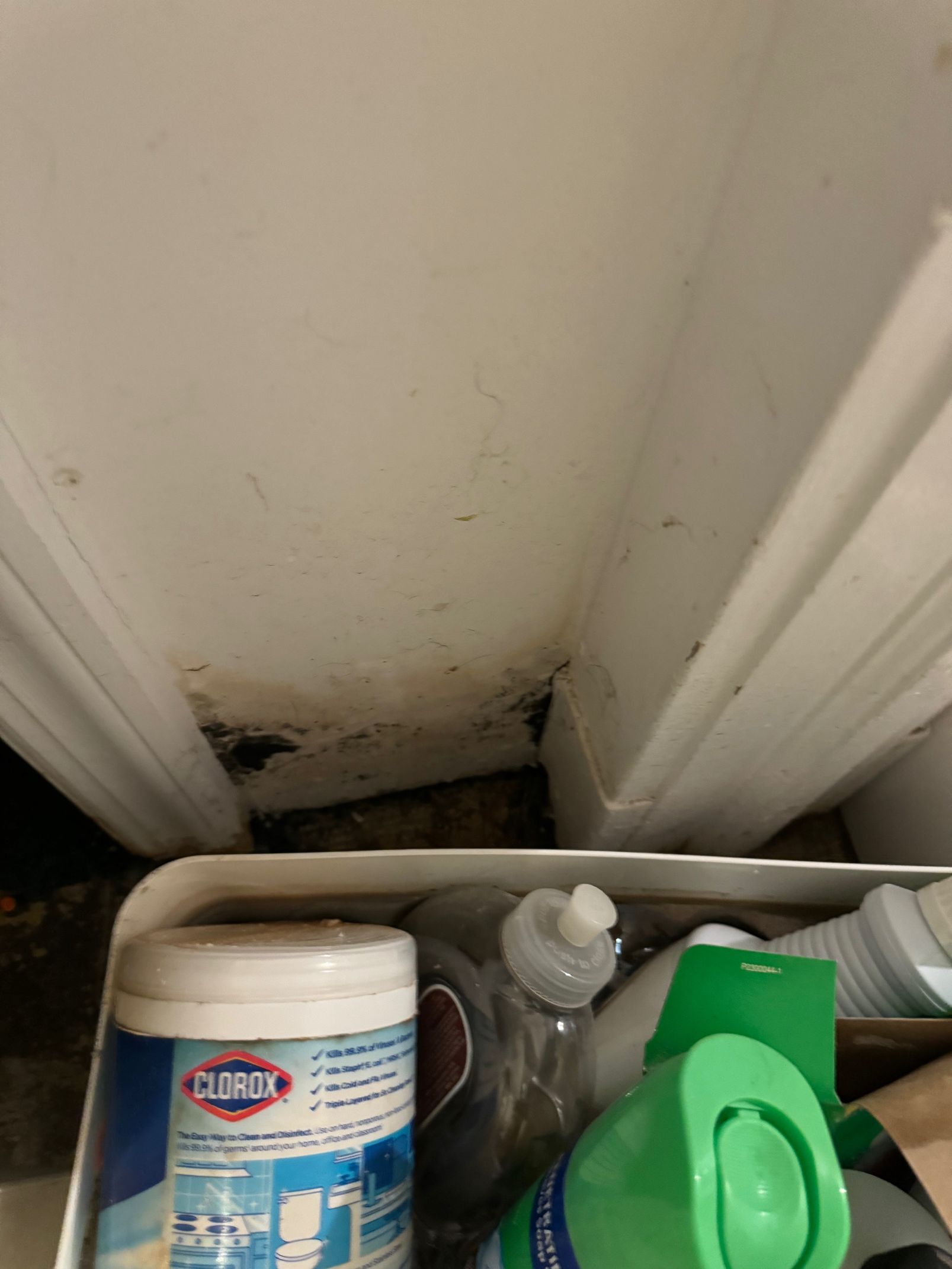 White framed opening with dark debris at bottom, above a white storage container with cleaning products.