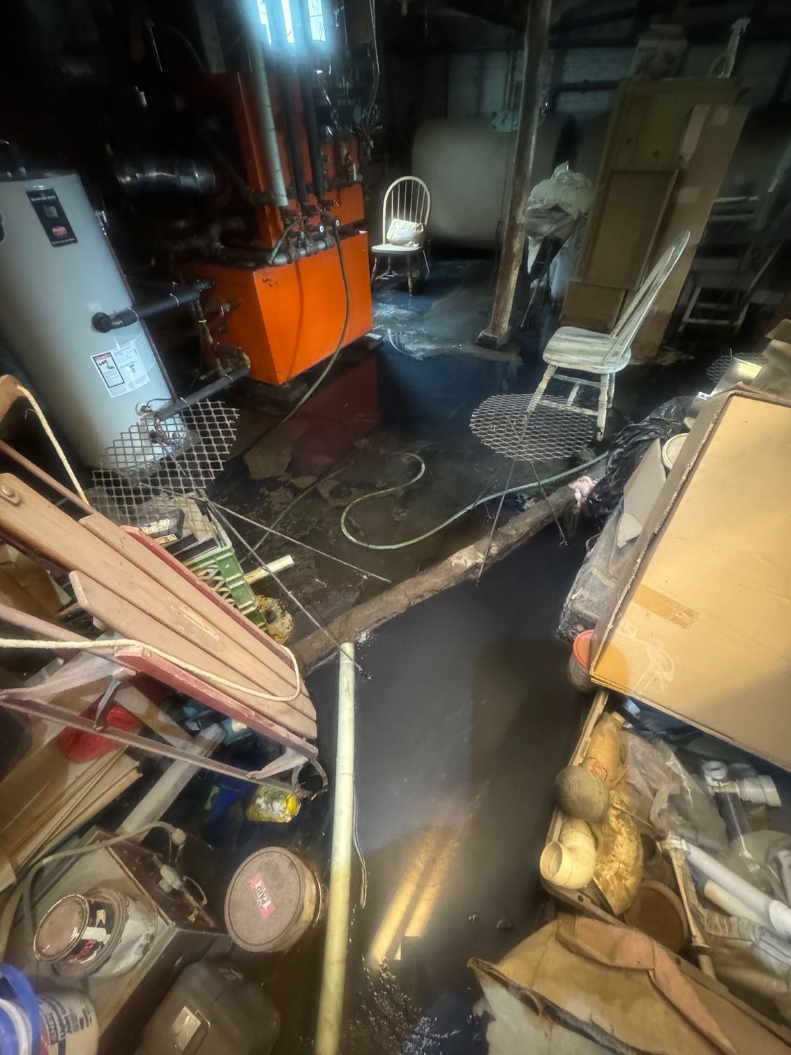 Flooded basement with equipment, furniture, and boxes submerged in water. Low light.