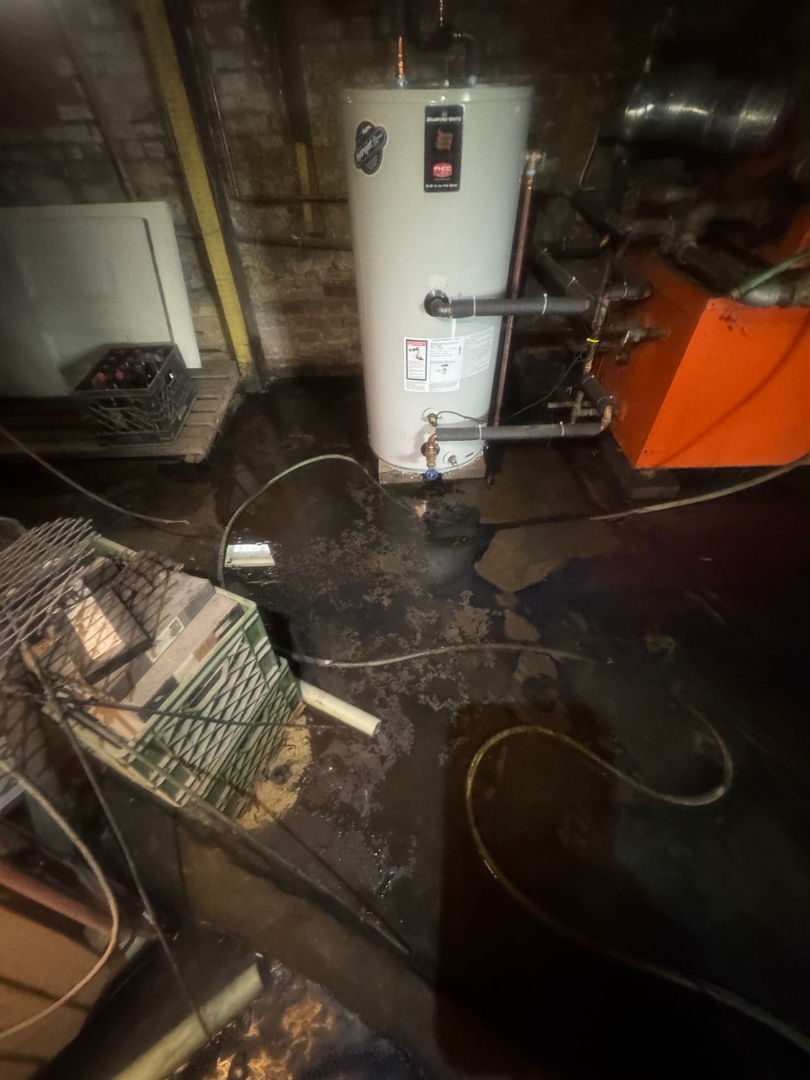Water heater in a flooded basement; pipes and electrical cords visible.